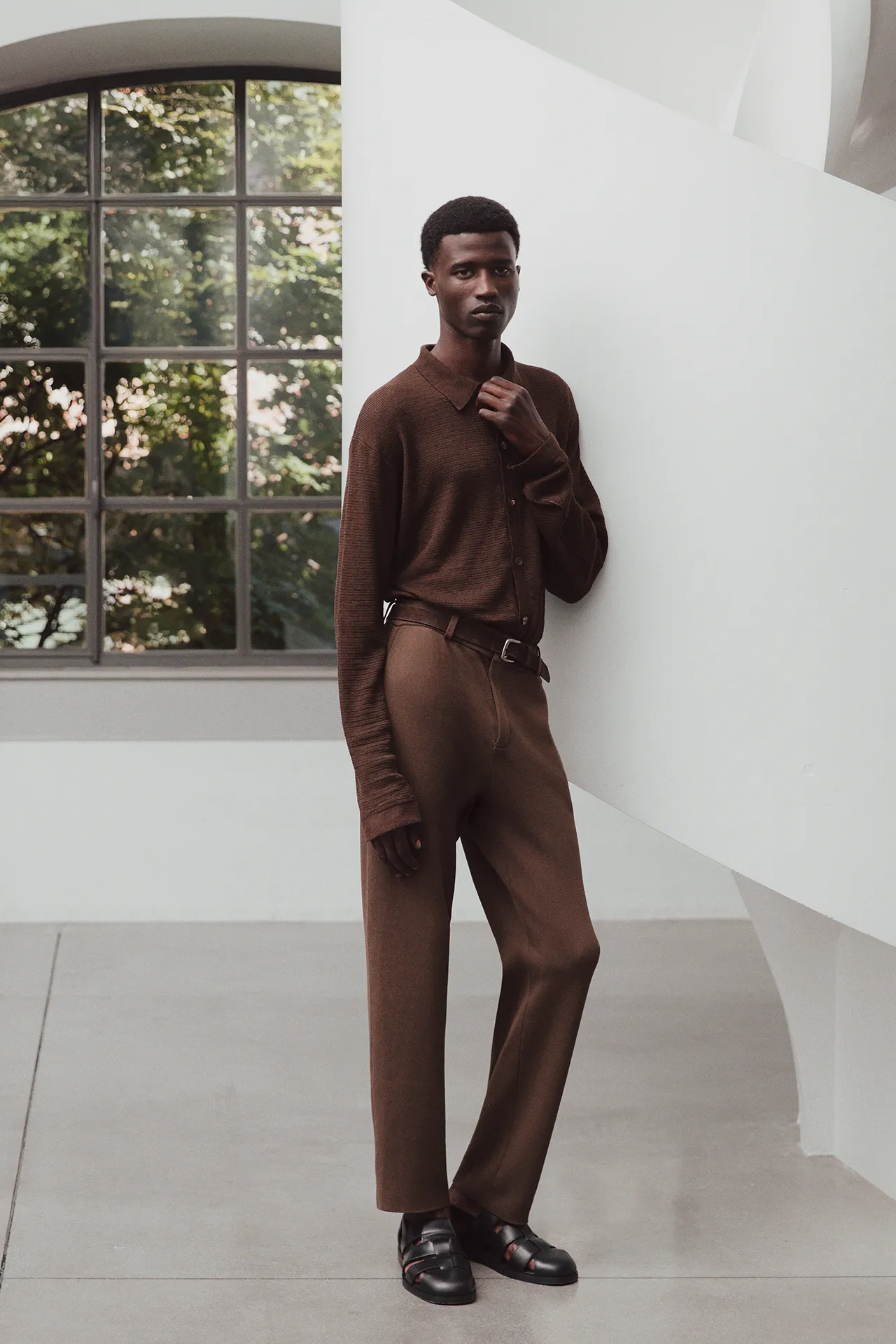 Full-length view of a male model wearing the Aida Barni SS26 collection brown fine-knit long-sleeve polo tucked into matching brown trousers.