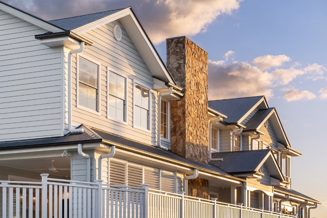 Exterior features of a Hamptons style house design in Brisbane, showcasing a textured stone chimney, crisp white weatherboards, and steep gables.
