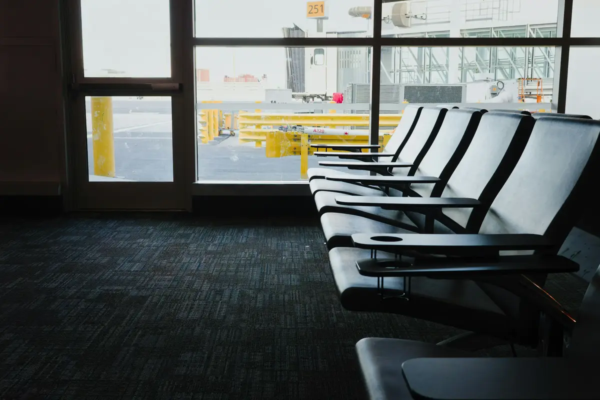 Empty airport waiting area with rows of chairs by large windows