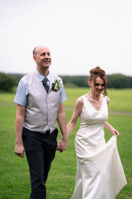 A bride and groom walking hand in hand across a grassy field