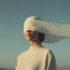 Surreal portrait of a woman wearing a cream top with a sheer white cloth draped over her eyes.