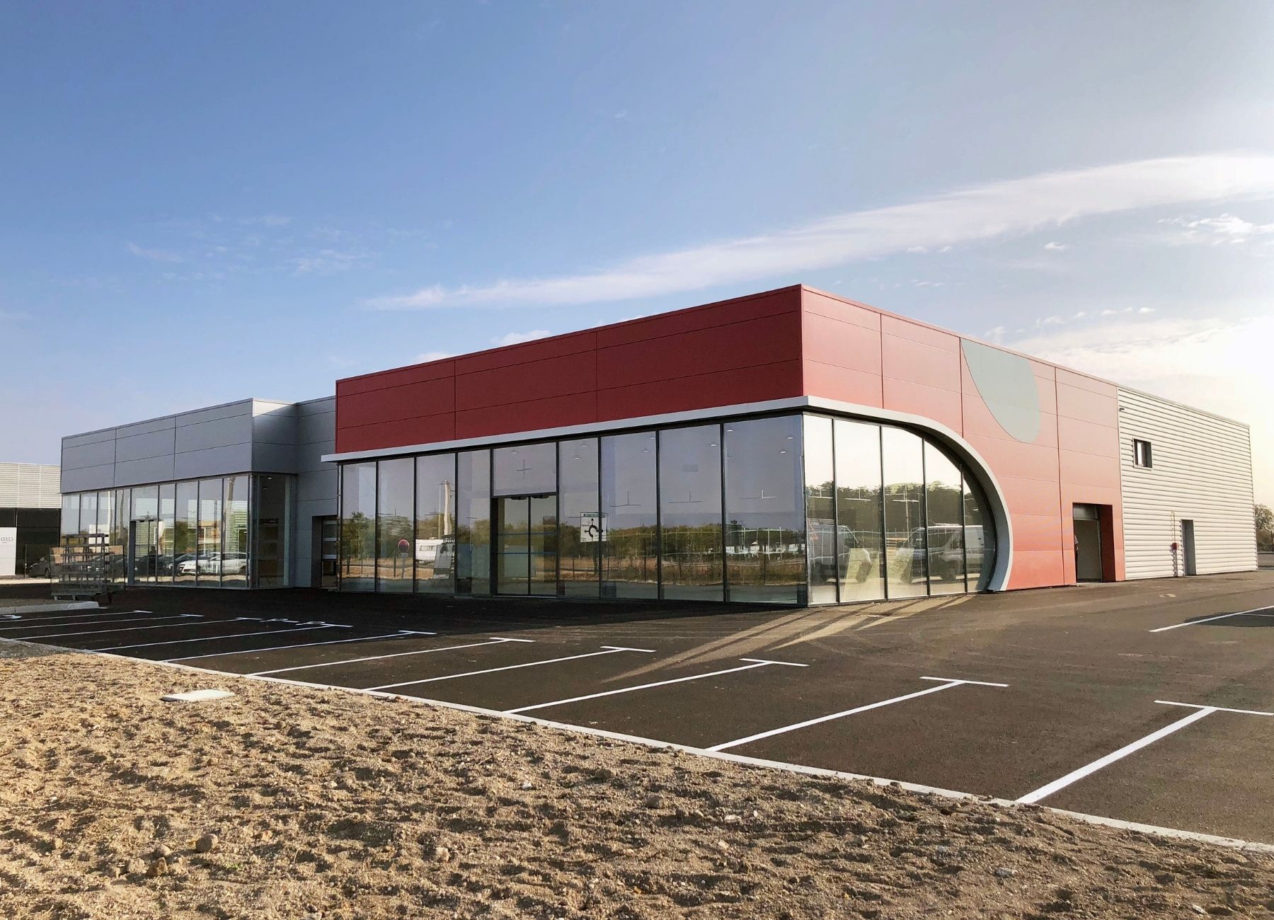 Autre angle du bâtiment commercial terminé avec bardage métallique clair et parking aménagé.