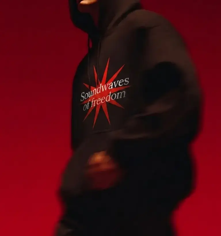 Dark hoodie printed with the Fusion starburst and the words Soundwaves of freedom, against a red background