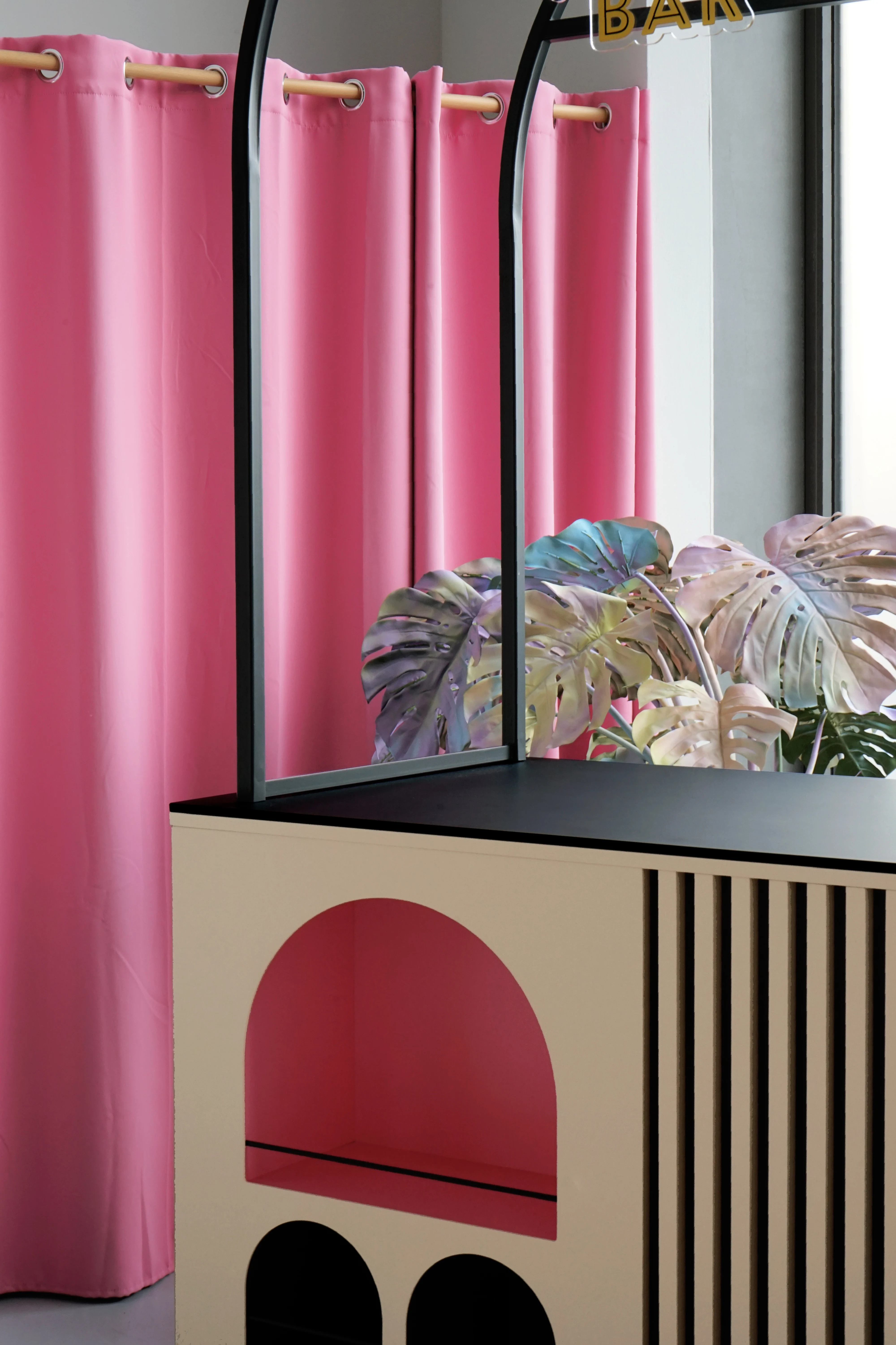 Side view of the BAILEYS Treatbar with arched cutout niches, pastel-colored monstera leaves and a pink curtain in the background.