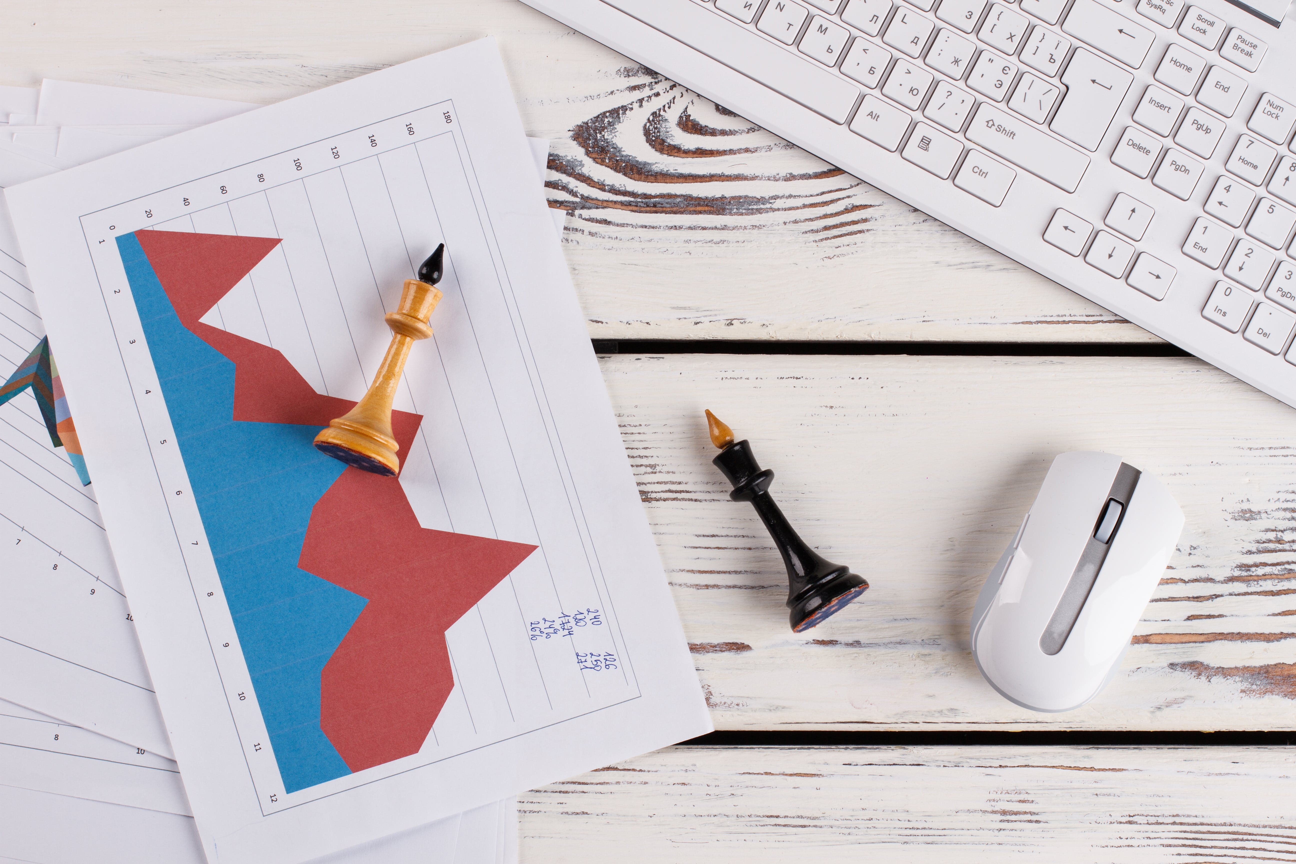Strategic business planning concept with chess pieces on financial graphs, keyboard, and mouse on wooden desk.
