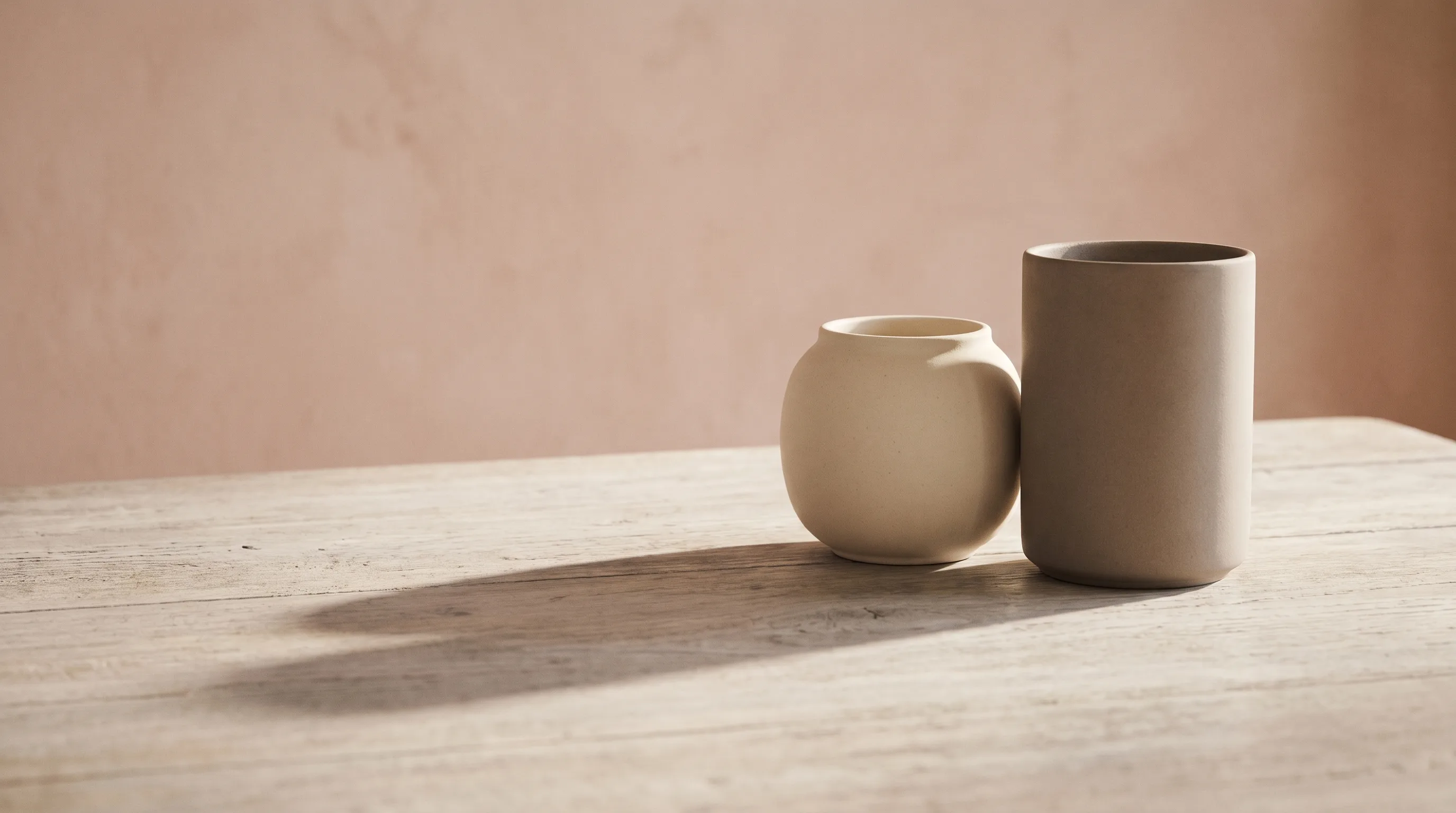 Two ceramic vessels of different shapes standing side by side, their two shadows merged into one
