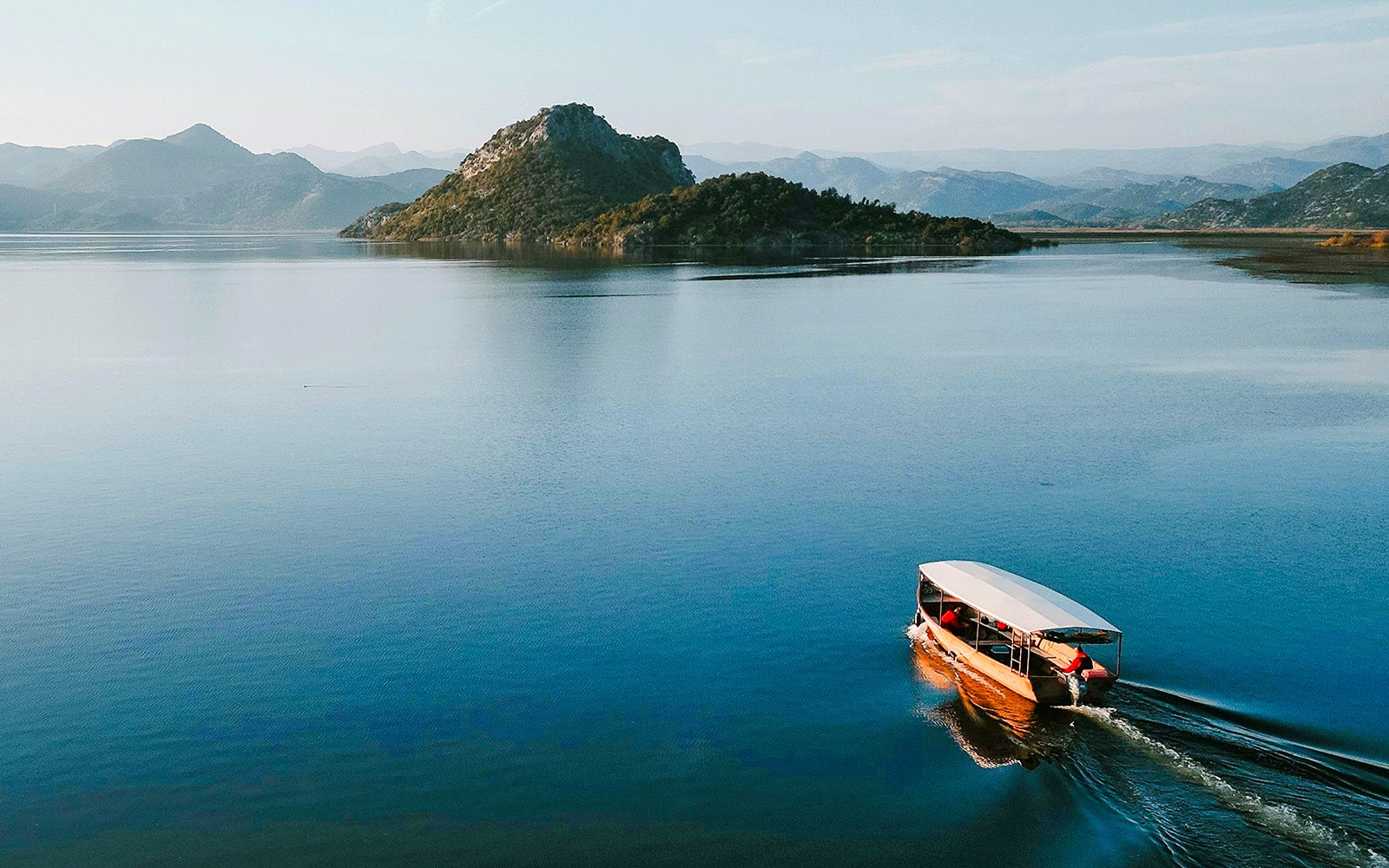 Прогулка на деревянной лодке по озеру Скадар с горным фоном.