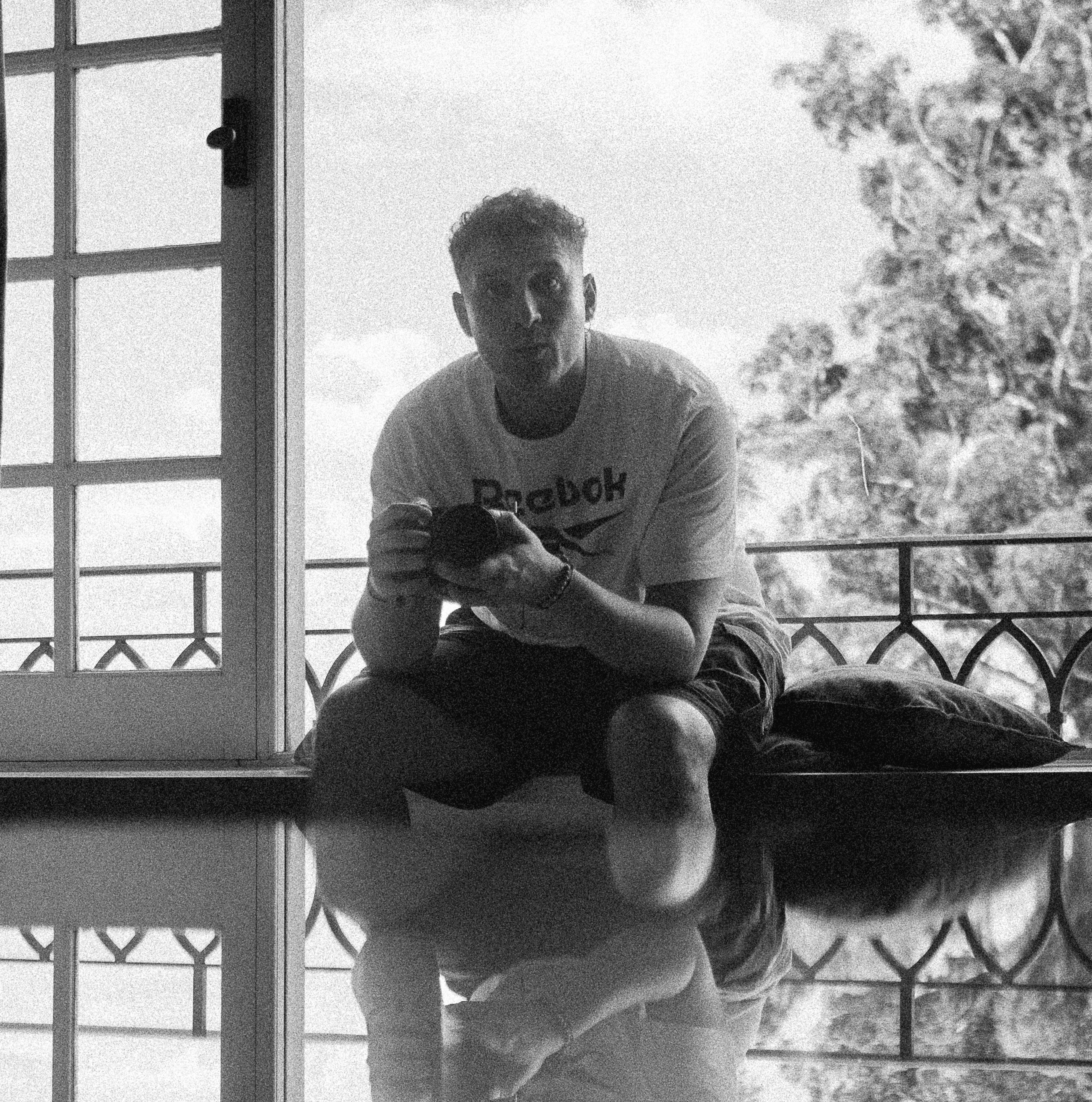 A thoughtful young person with dark hair gazes to the side, captured in soft black and white lighting.