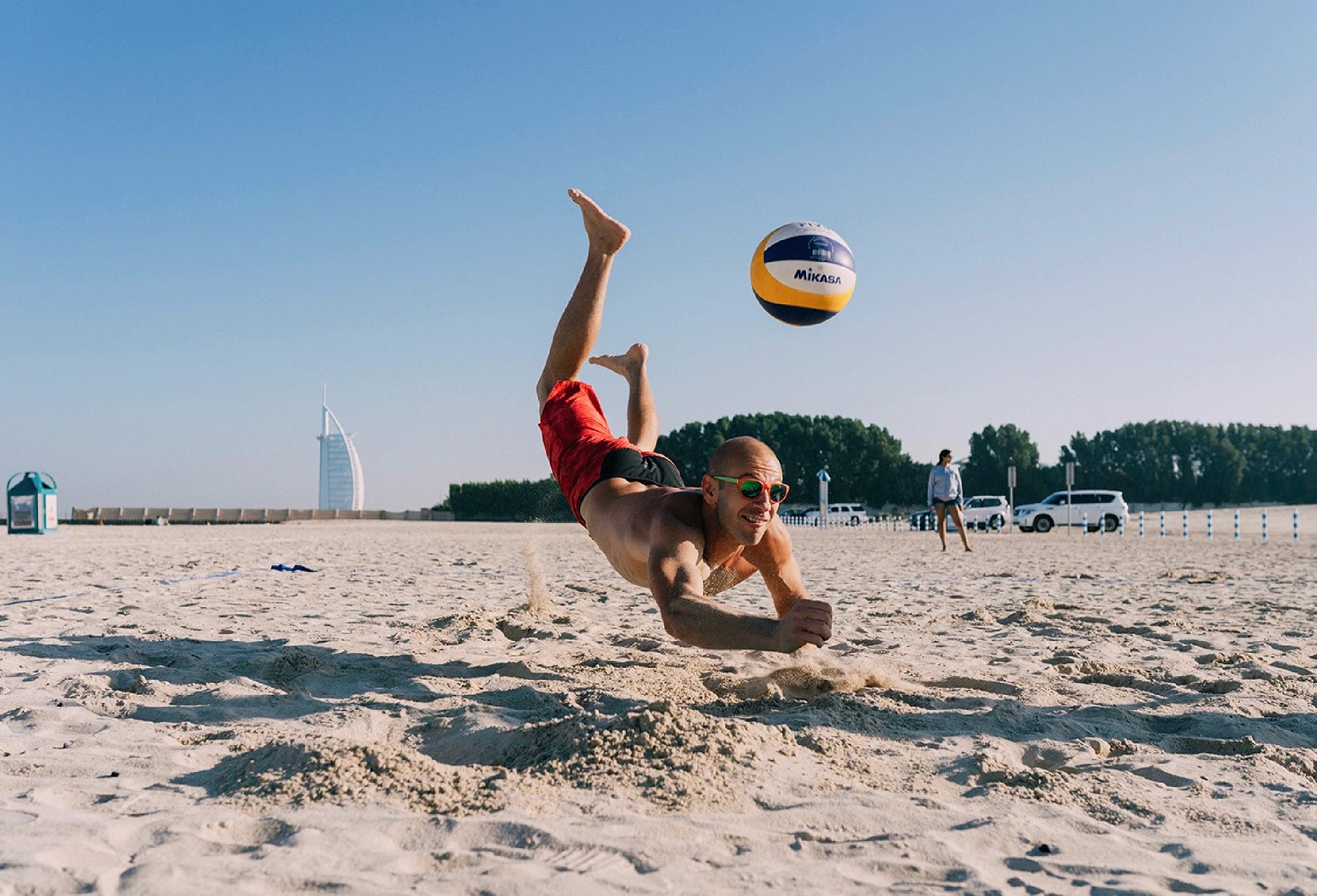 A male jumping into the sand to catch the falling volleyball