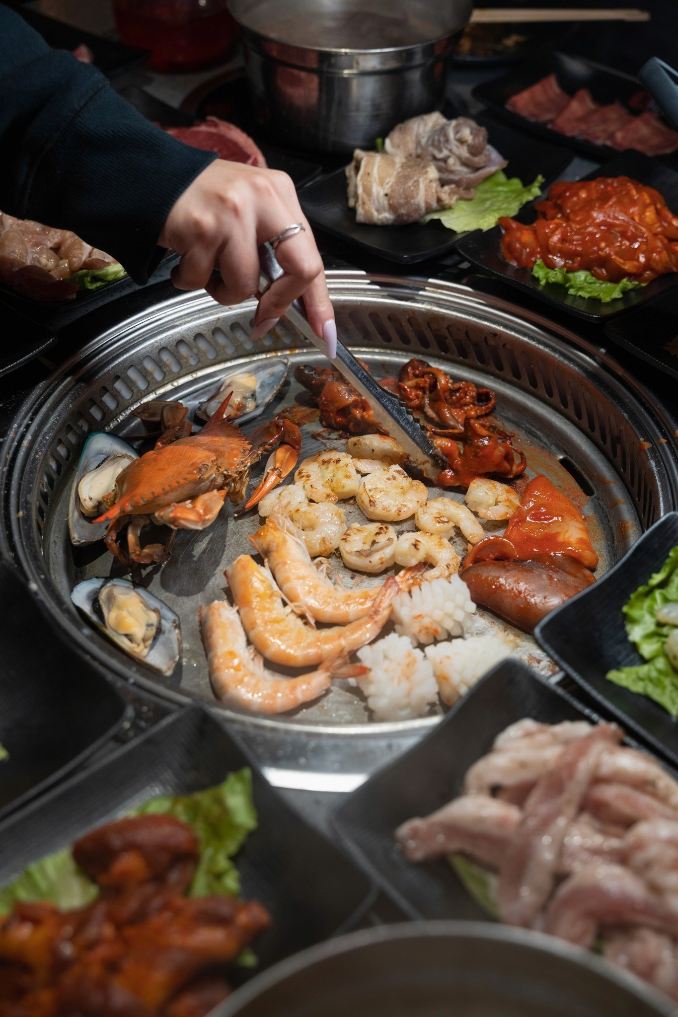 "Close-up of marinated meats grilling on a tabletop barbecue at KPOT, showcasing their signature flavors and interactive dining experience."