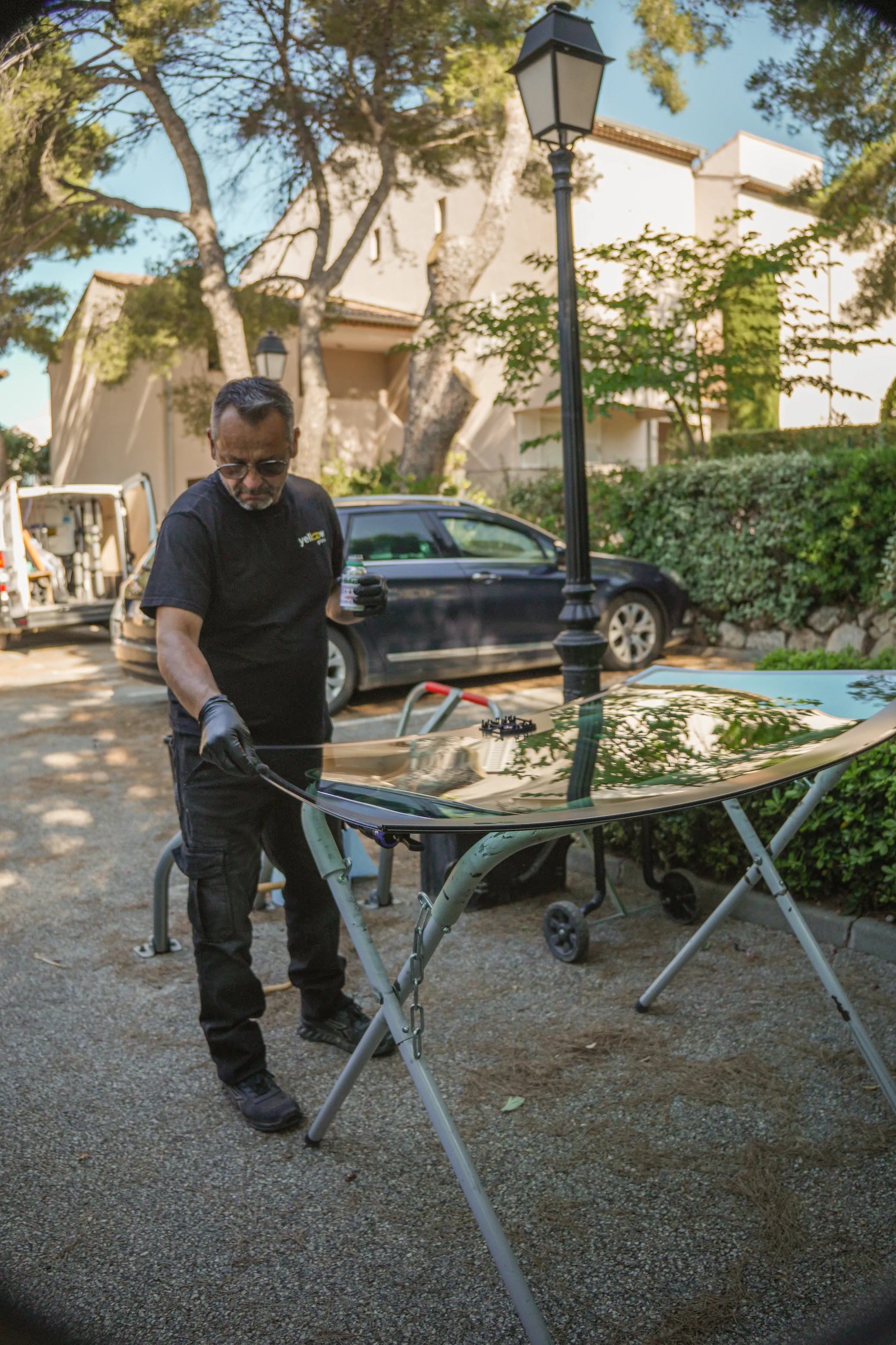 Un homme répare un pare-brise de voiture à l'extérieur, près d'une voiture.