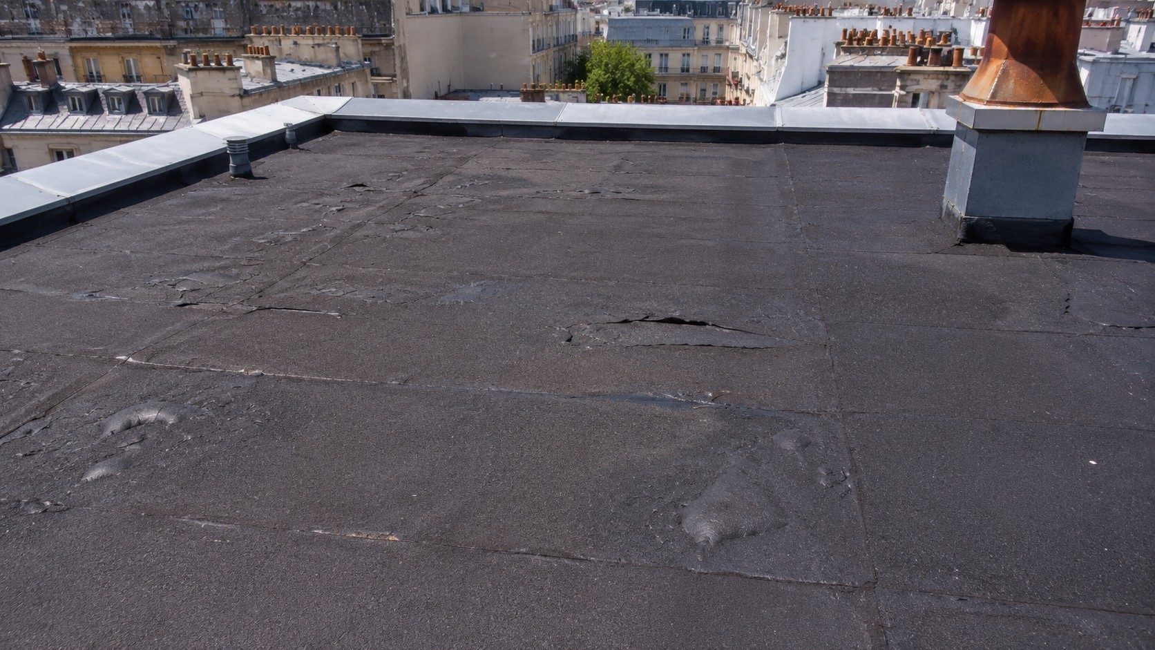 Photo documentaire d’une toiture-terrasse en bitume à Paris, avec cloques, fissures et zones décollées visibles sur la membrane d’étanchéité après de fortes chaleurs estivales.