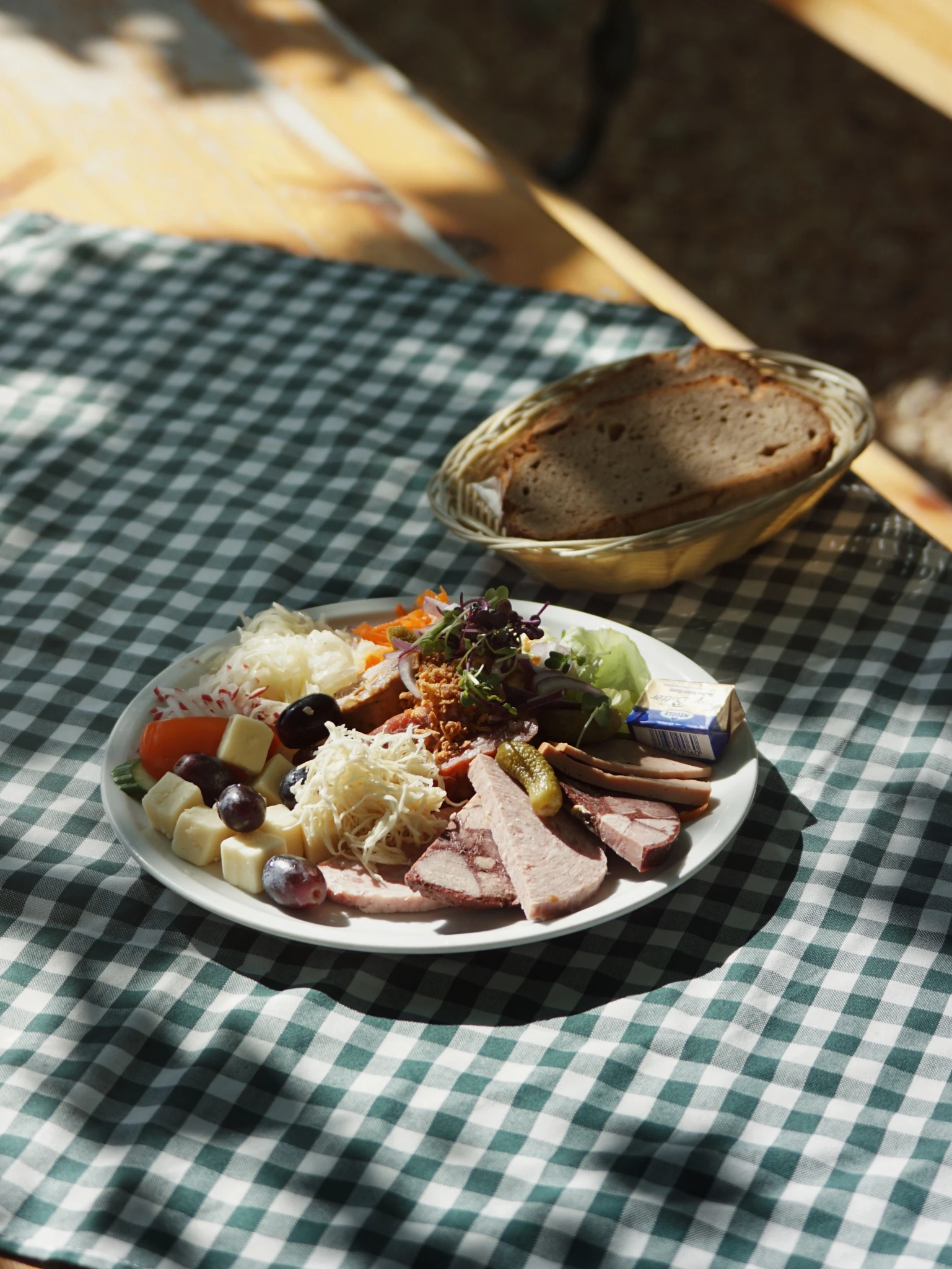 Brotzeitplatte mit Käse und Wurst, daneben Korb mit frischem Brot