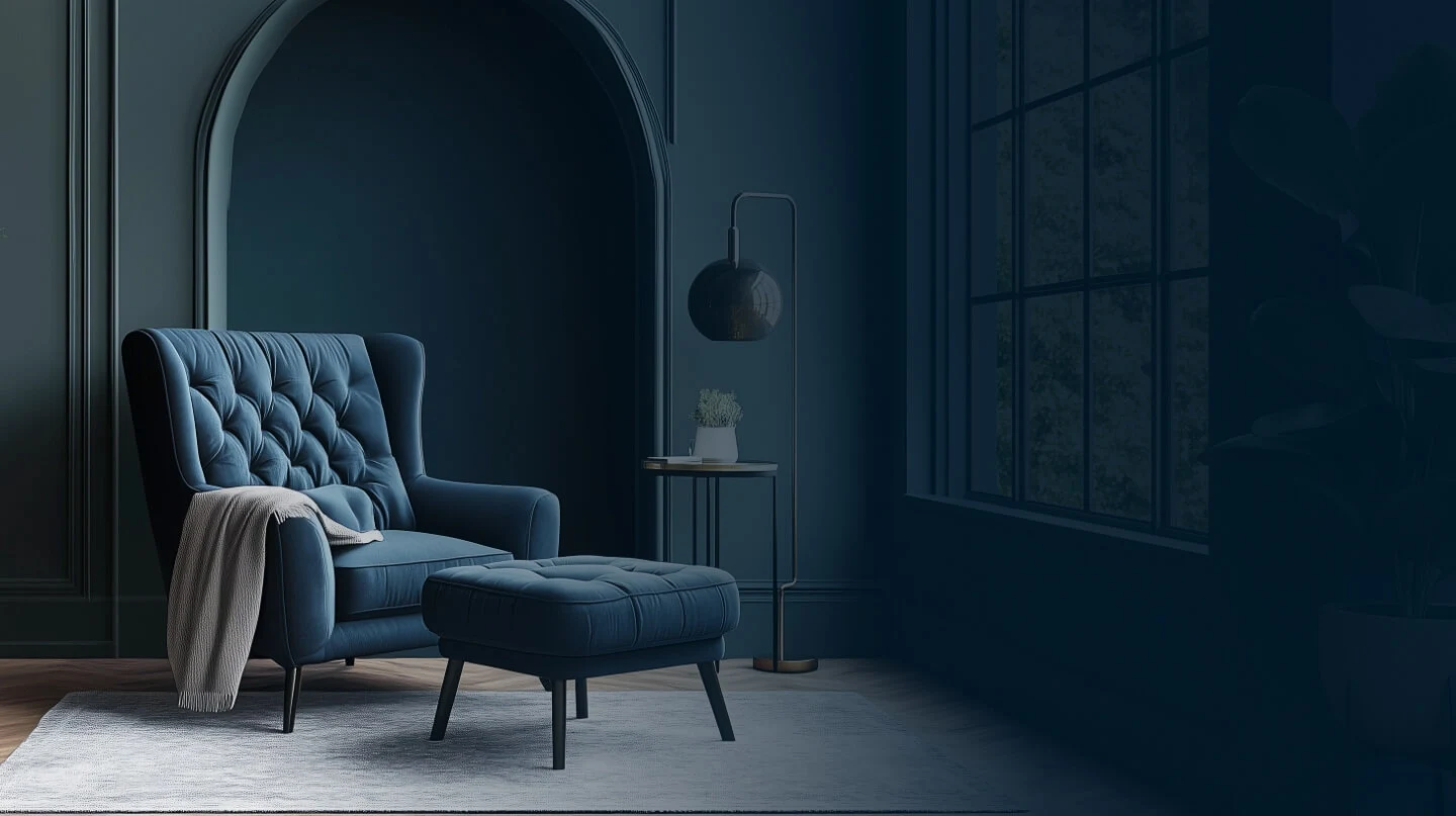 Elegant reading nook with a deep blue tufted armchair, matching ottoman, side table, and modern lamp against a dark arched wall