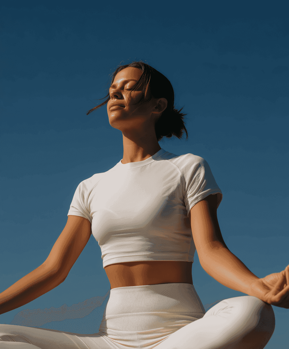 Woman in white athletic wear meditating against a blue sky.