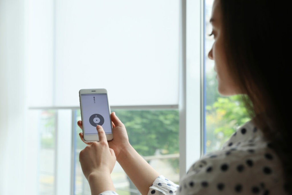 Woman using mobile device to control motorized blinds