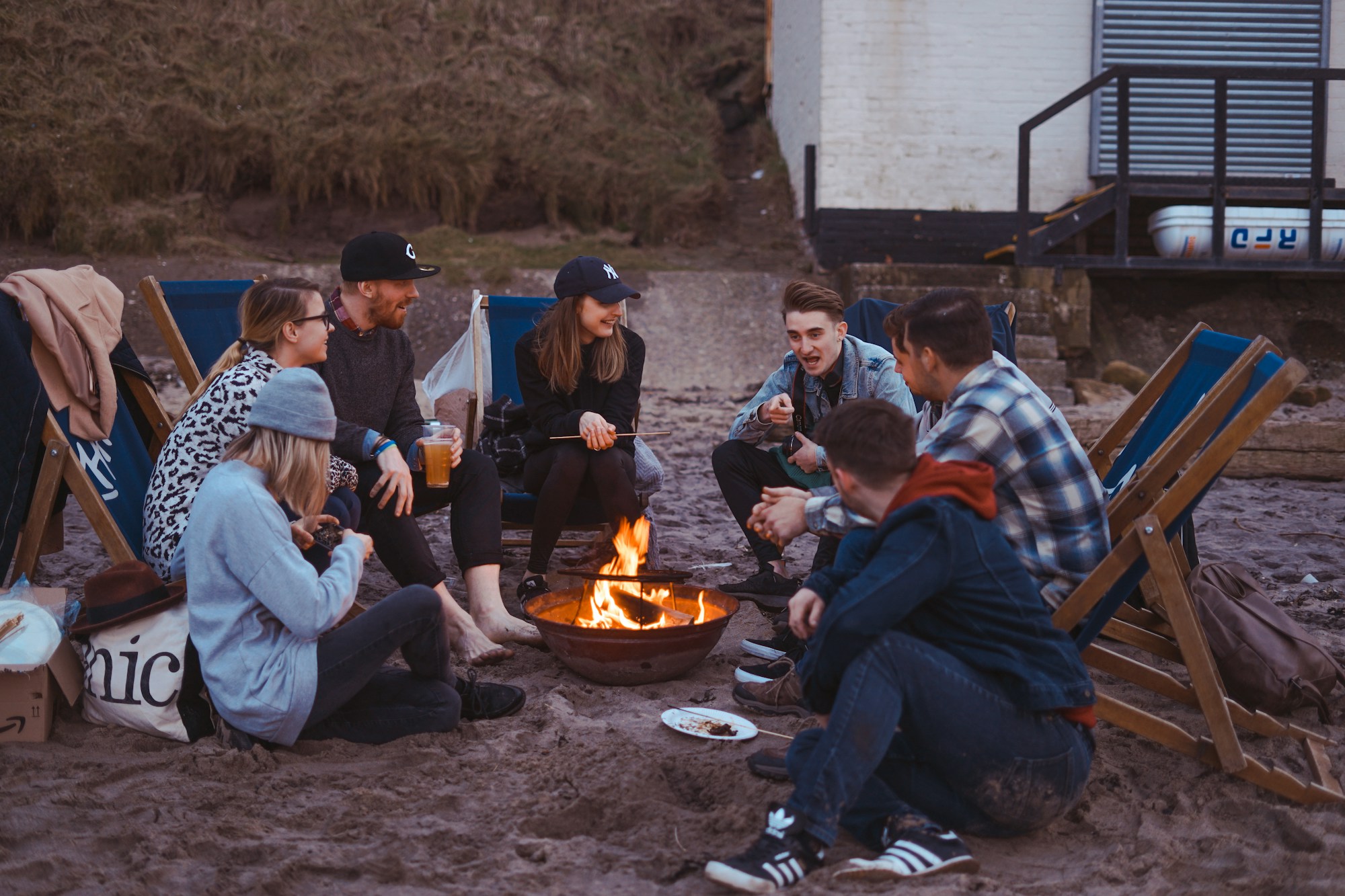 Group of friends sitting around a fire pit on a beach at dusk