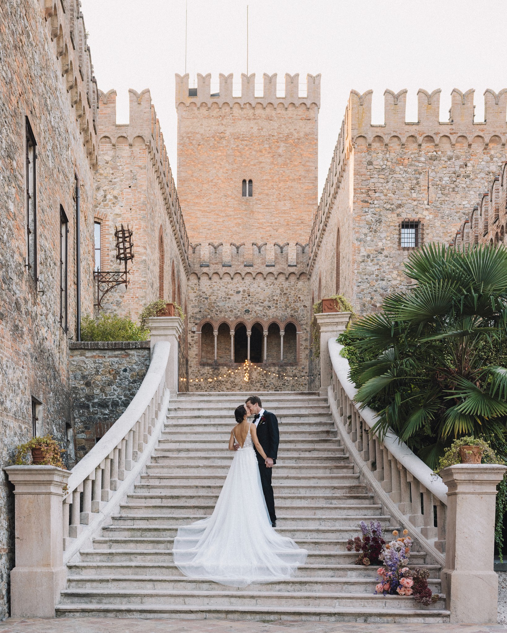 Sposi sulla scalinata del Castello di Tabiano, lei in abito bianco con strascico, lui in abito scuro tra muri medievali