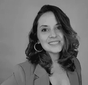 Minimal studio portrait of a confident woman in a white shirt, arms crossed, on a soft gray background.