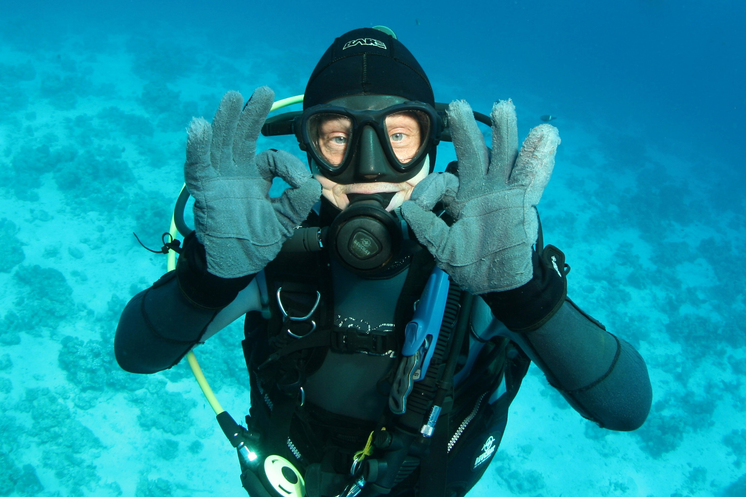 A diver underwater in front of a coral reef gives the okay hand signal