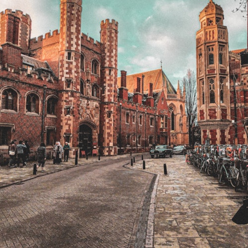 鹅卵石街道两旁是历史悠久的红砖建筑和自行车,背景中有行人和一辆停放的汽车。