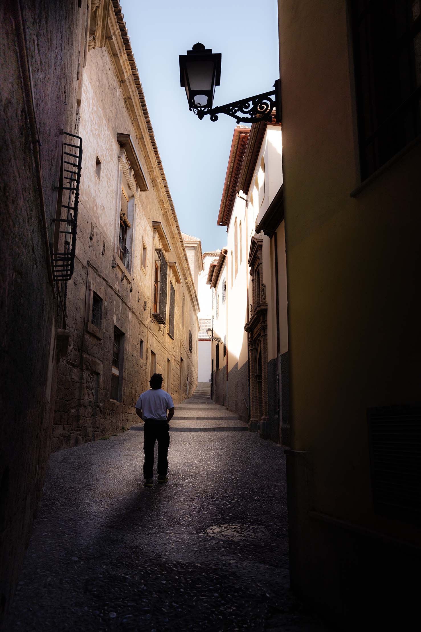 Alleyway in Granada, Spain with a person standing in the middle, sunlight hitting the building tops.