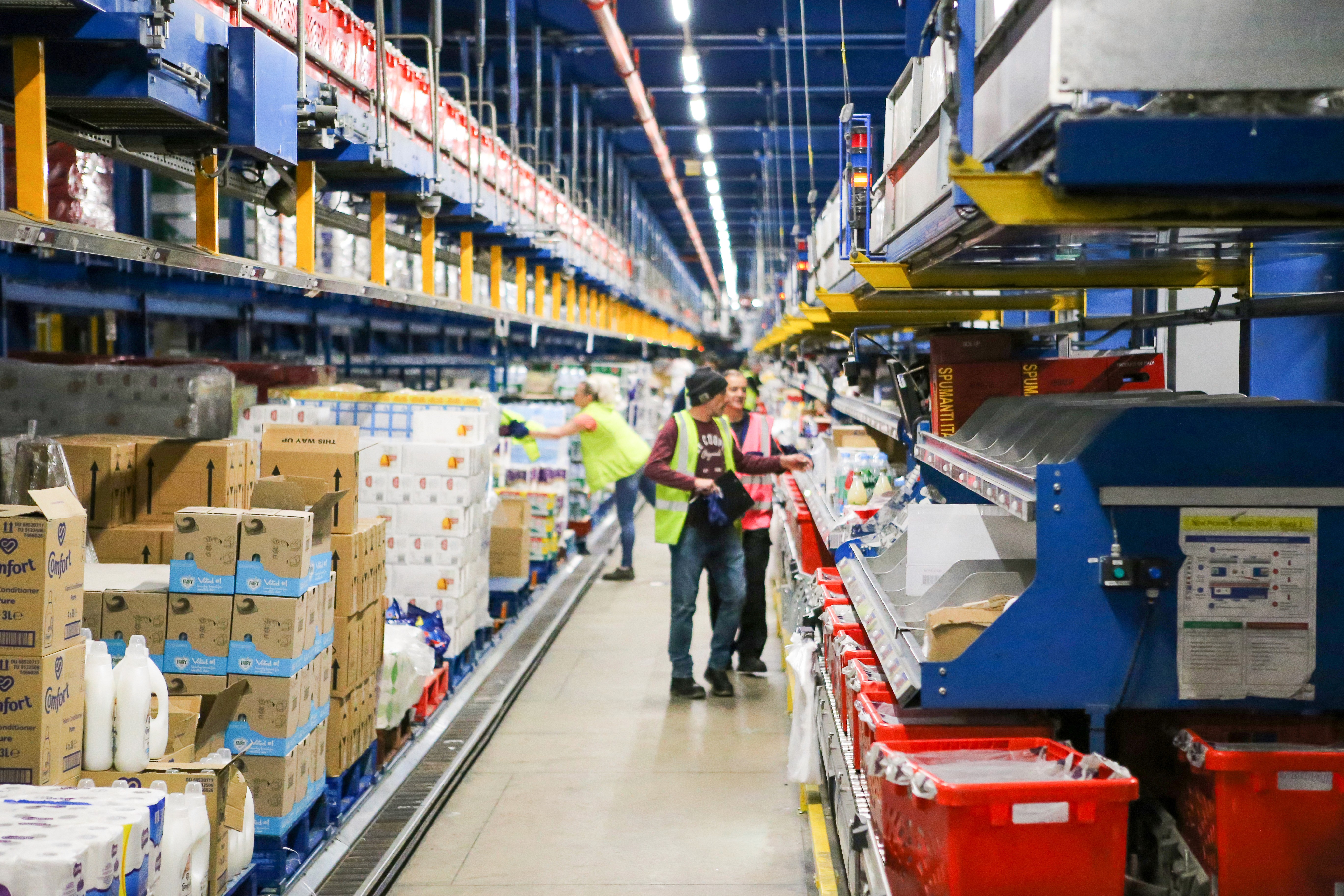 People in a warehouse aisle, with products stocked to the left and order crates on the right ready for customer orders