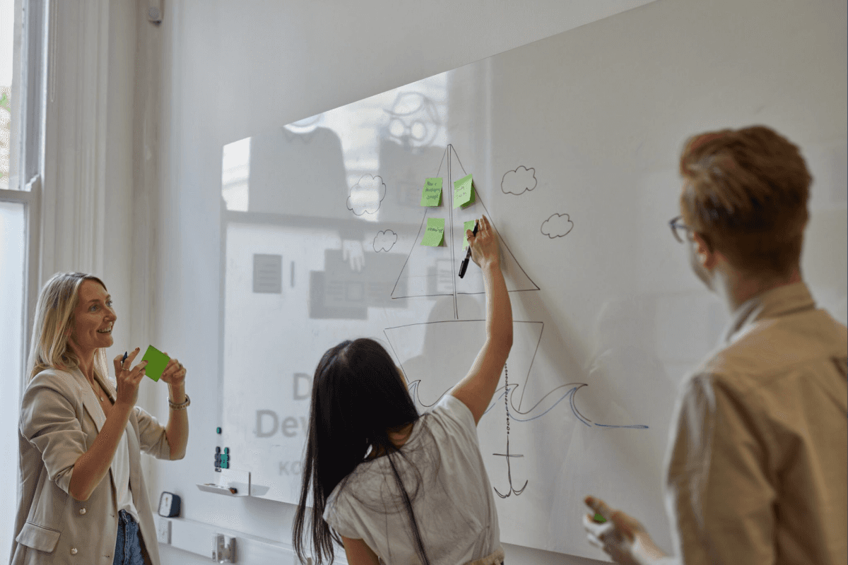 A designer writing notes on a whiteboard with a sketch of sailboat in the background