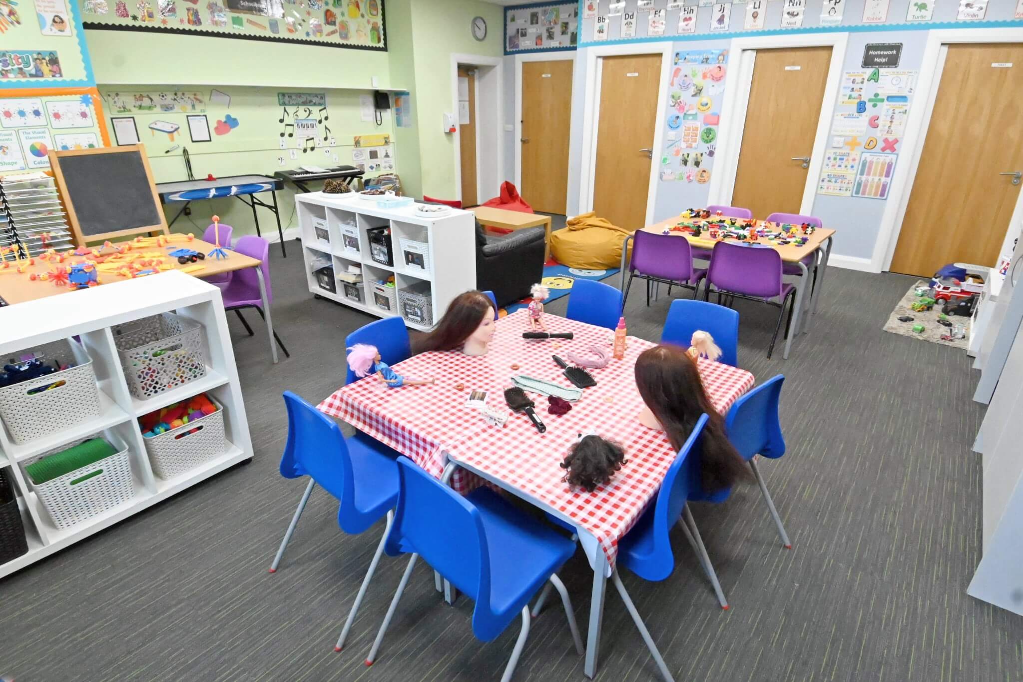 Bright classroom with children's art on walls, play tables, and storage shelves.