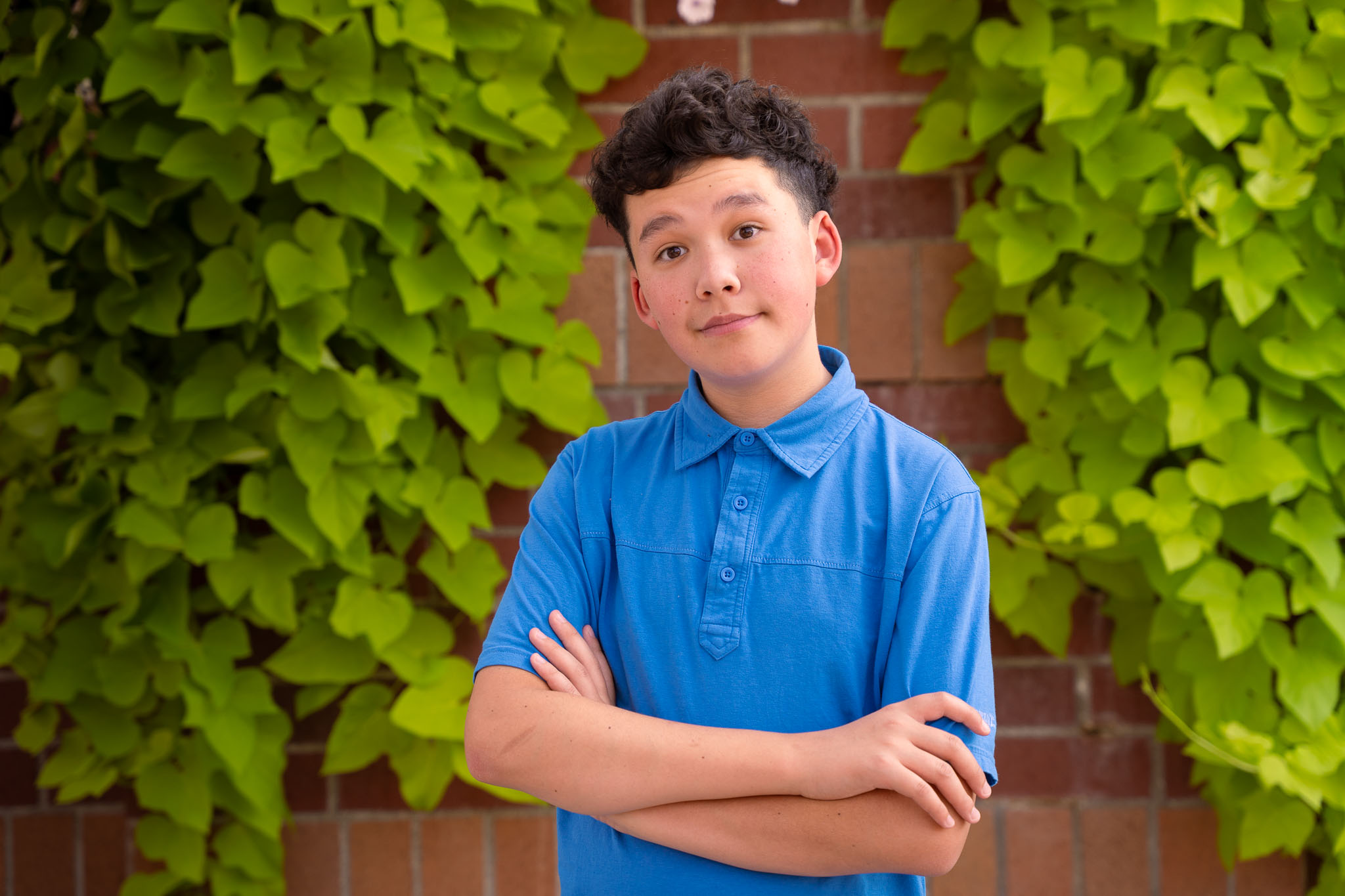 A portrait of a young boy with a brick wall behind him in green fully edged draping over the brick wall