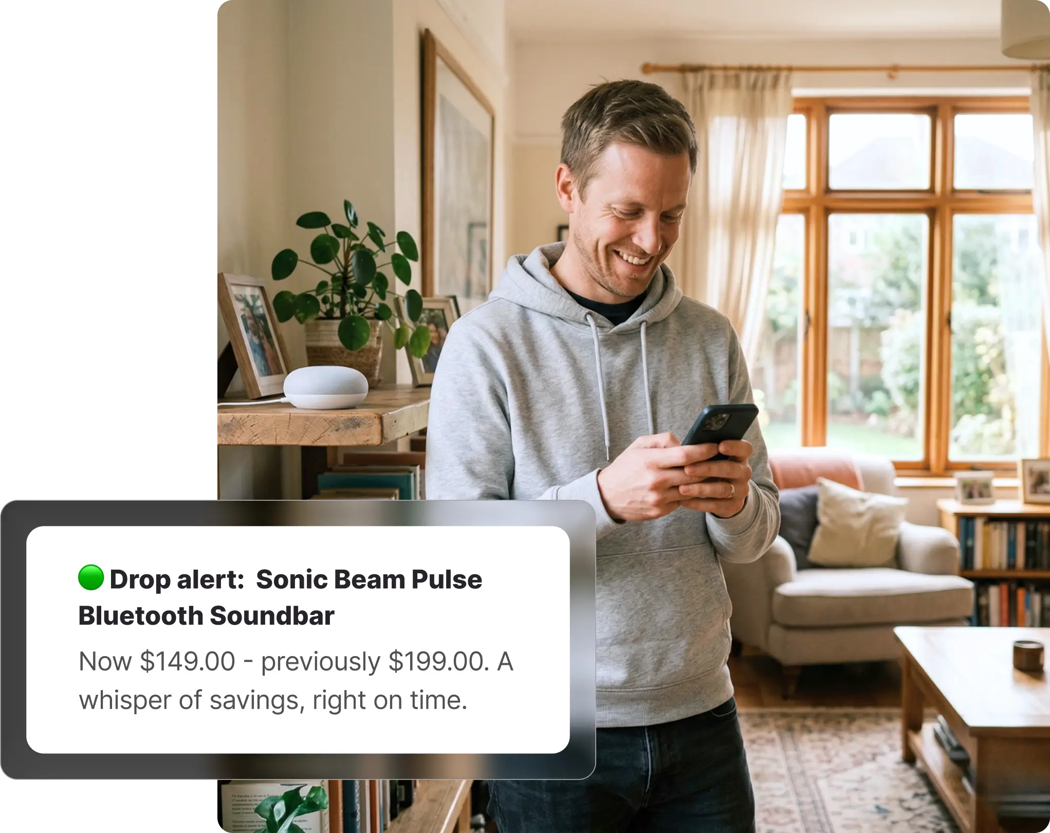 Man in a grey hoodie standing in a living room smiling at his phone, receiving an Amazon price drop alert for a Bluetooth soundbar on Whisprice, with a smart speaker and indoor plants visible on a shelf behind him.