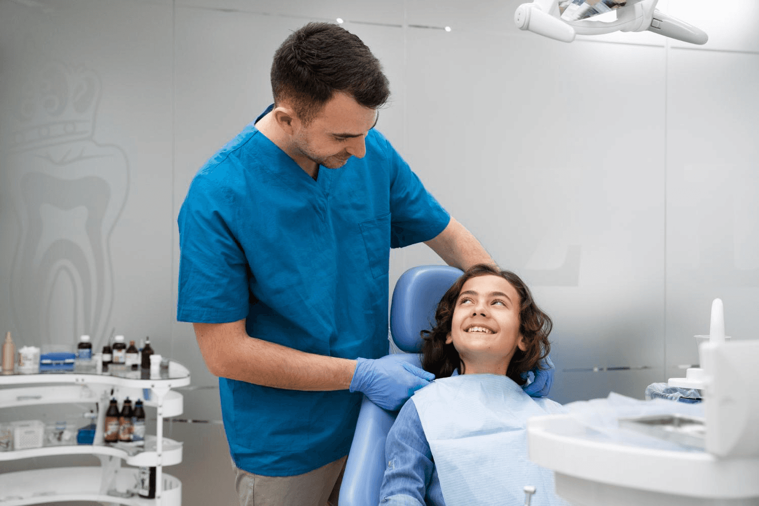 A young girl sitting in a dental chair, receiving dental treatment from a dentist and dental assistant.