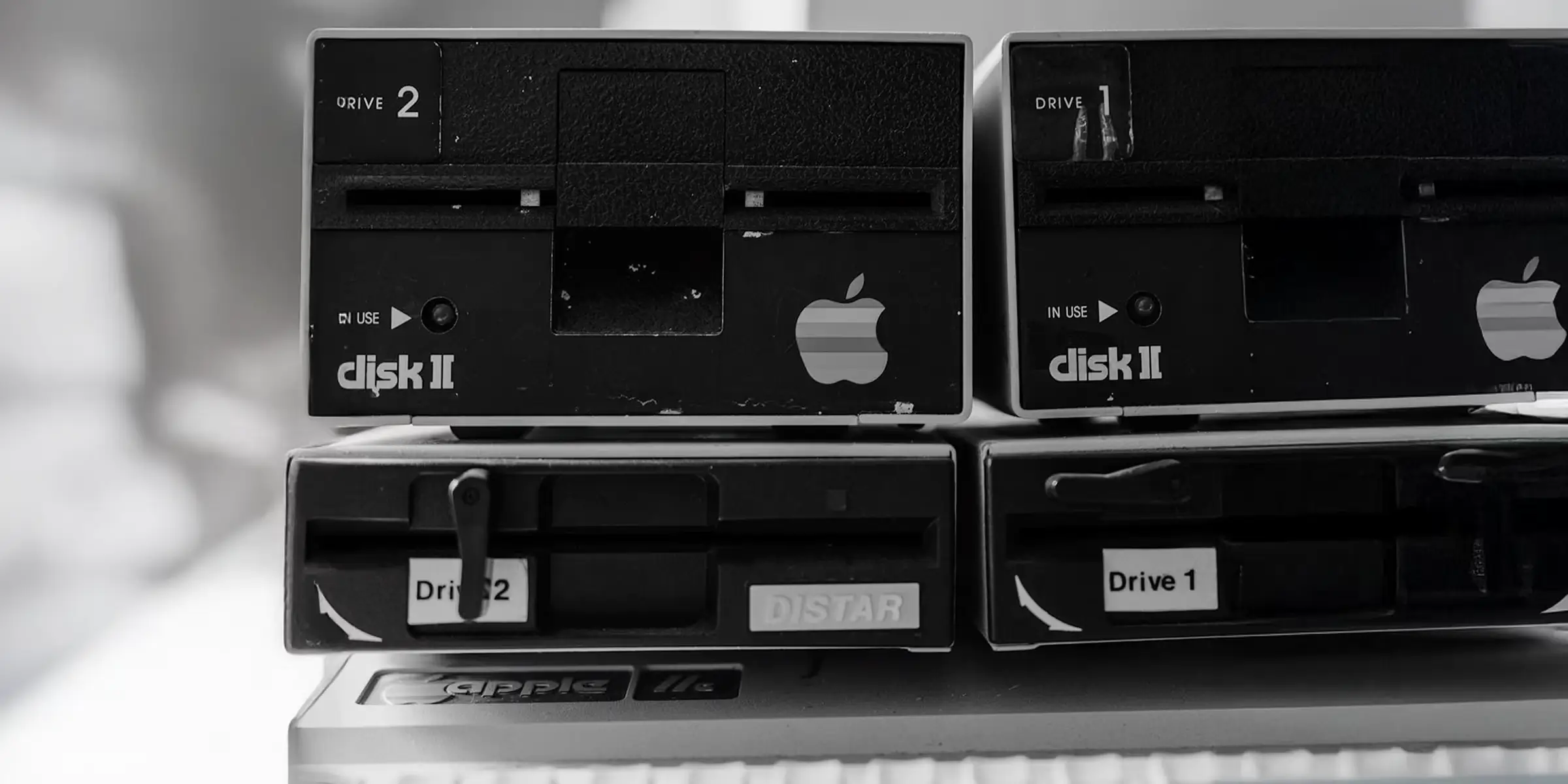 Black and white close-up of vintage computer disk drives with an Apple logo, suggesting legacy, consistency, and brand recognition over time.