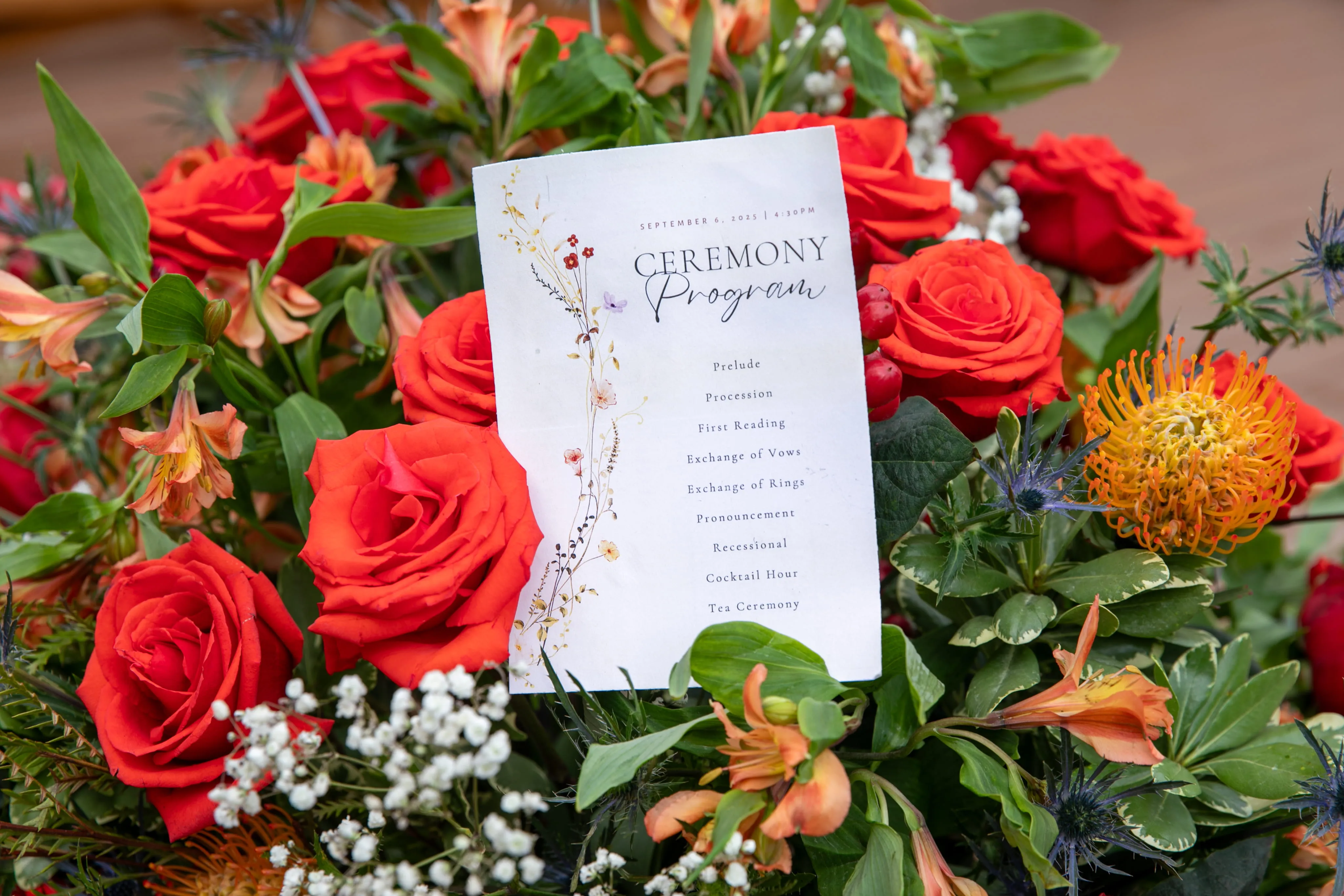 Wedding ceremony program surrounded by red roses at Camp Lenox