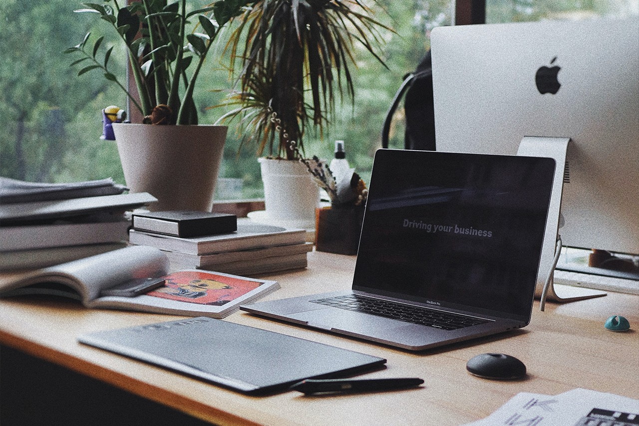 Laptop on a desk, surrounded by a graphics tablet, books, another computer and plants