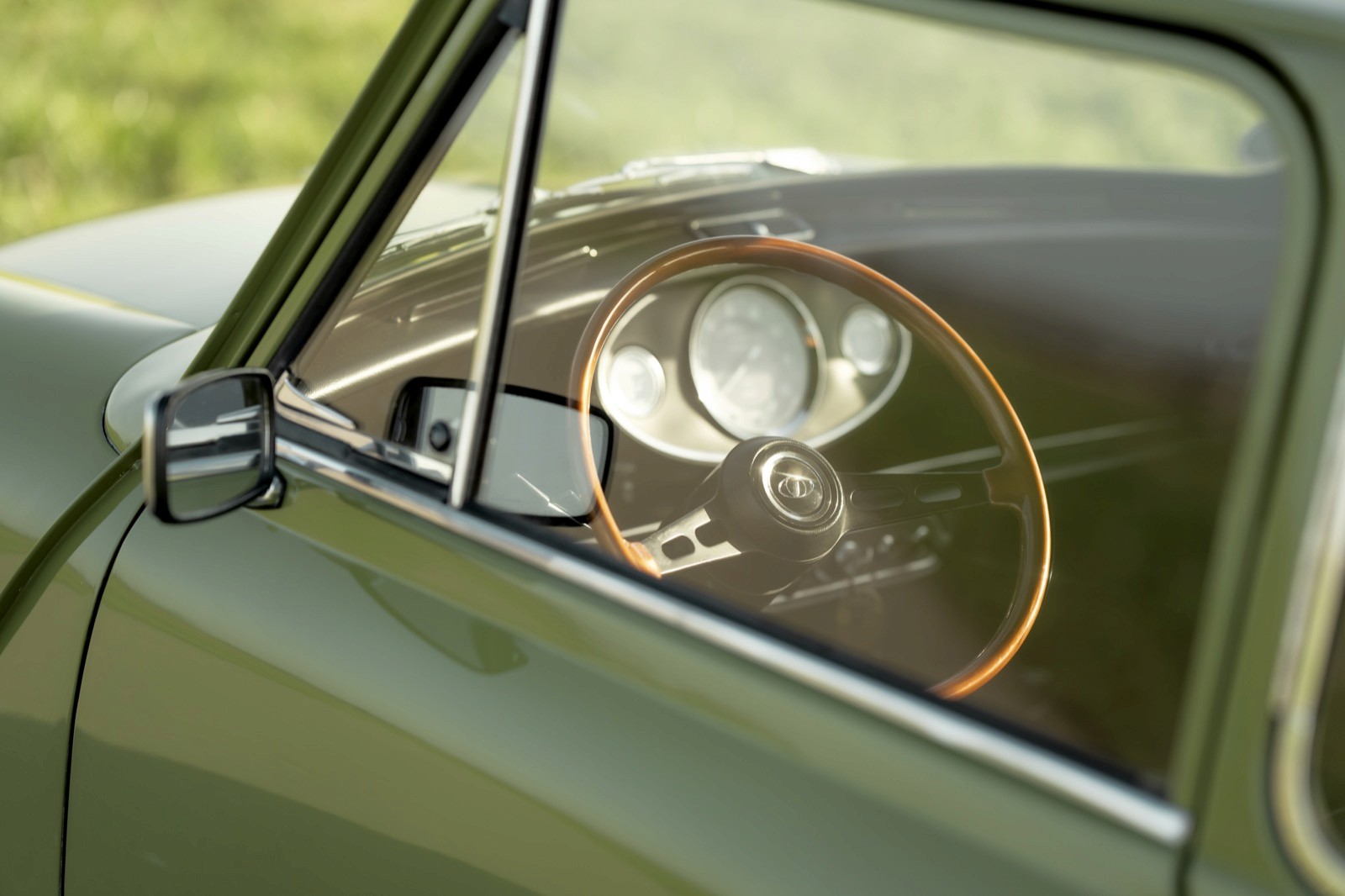 Close-up of a vintage car's steering wheel and dashboard visible through the driver’s side window.