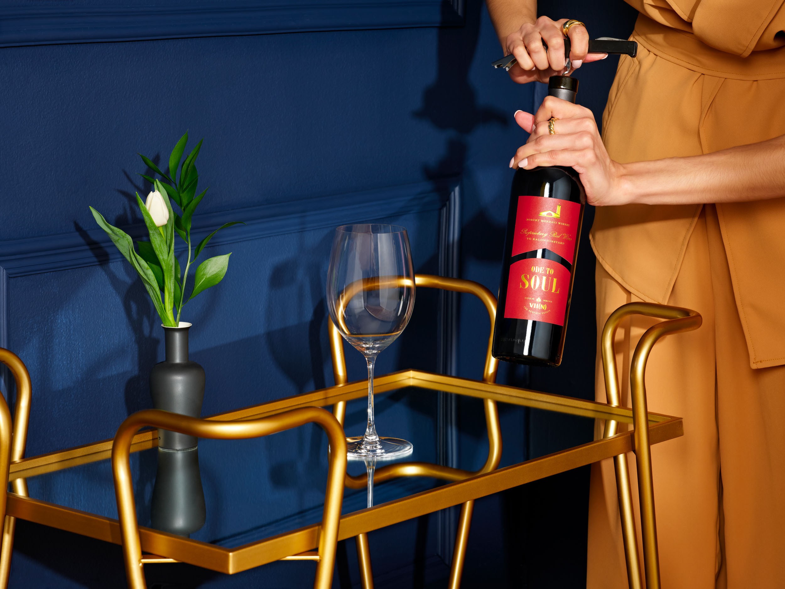 Ode to Soul wine bottle being opened above a brass bar cart against a deep navy wall