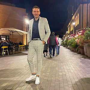Black-and-white portrait of a man with an afro in motion, wearing a hoop earring and chain necklace, against a light gray background.