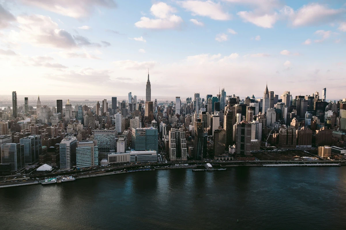 New York City skyline across the East River, with the Empire State Building centered under a bright sky.
