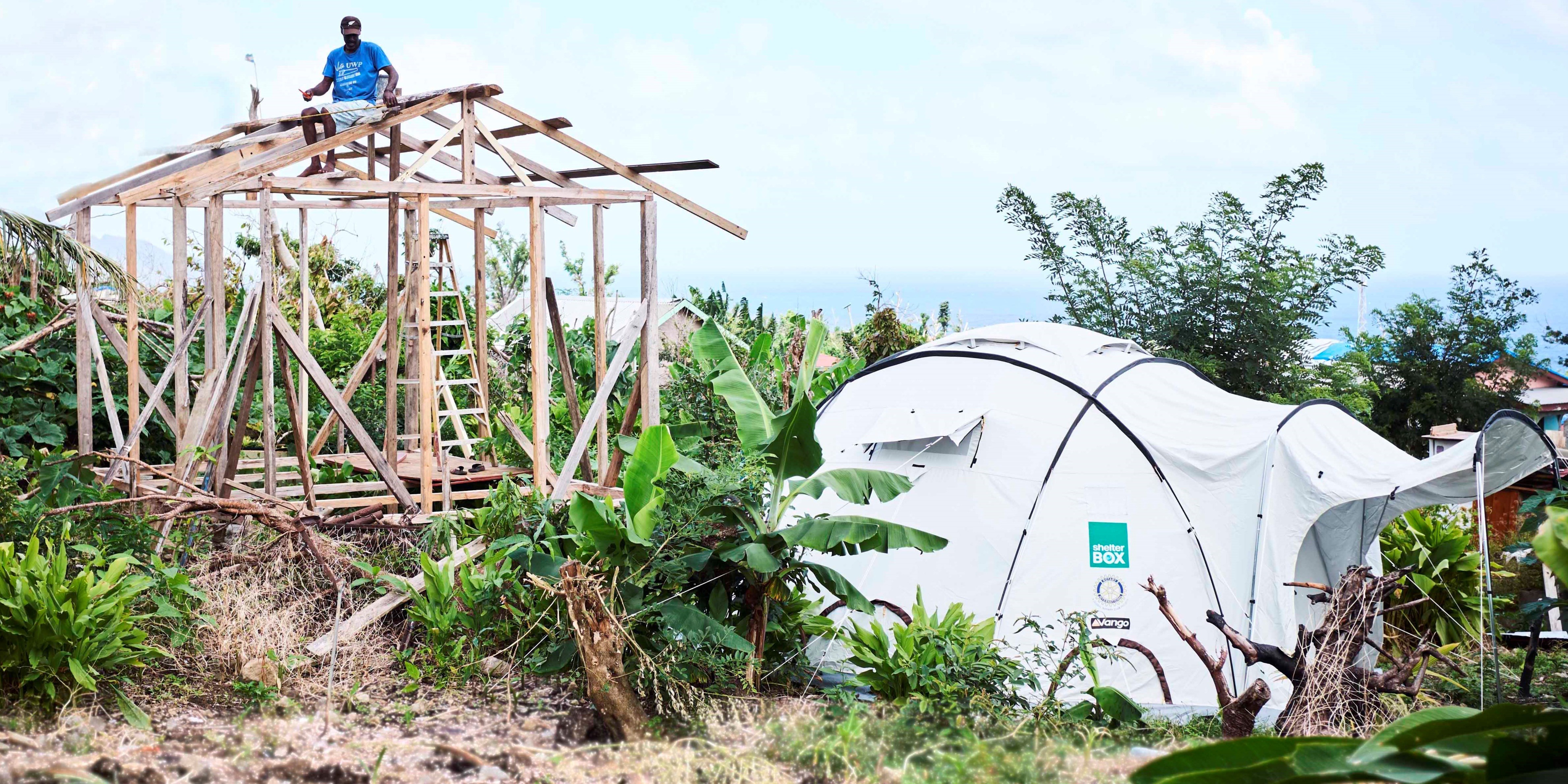 Decorative image of a Shelterbox tent as a volunteer rebuilds in a lush green setting