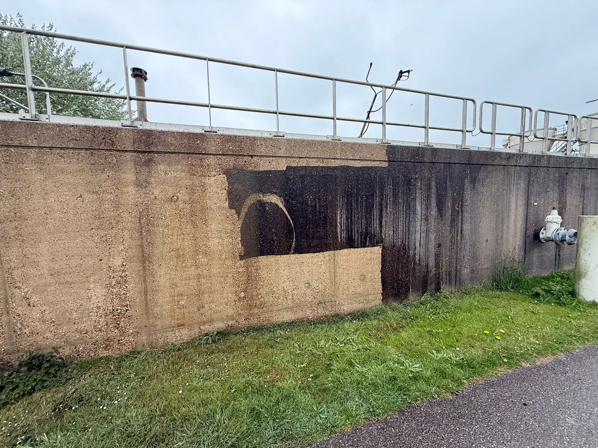 Betonnen gevel na reiniging met heet water, met het gereinigde lichte deel naast het nog vervuilde donkere deel