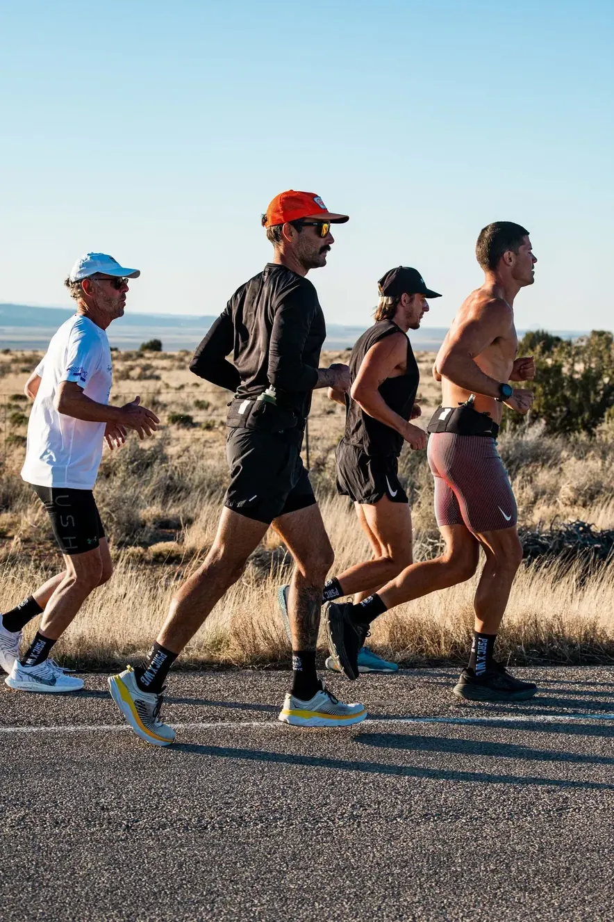 Four runners jogging together along a desert road.