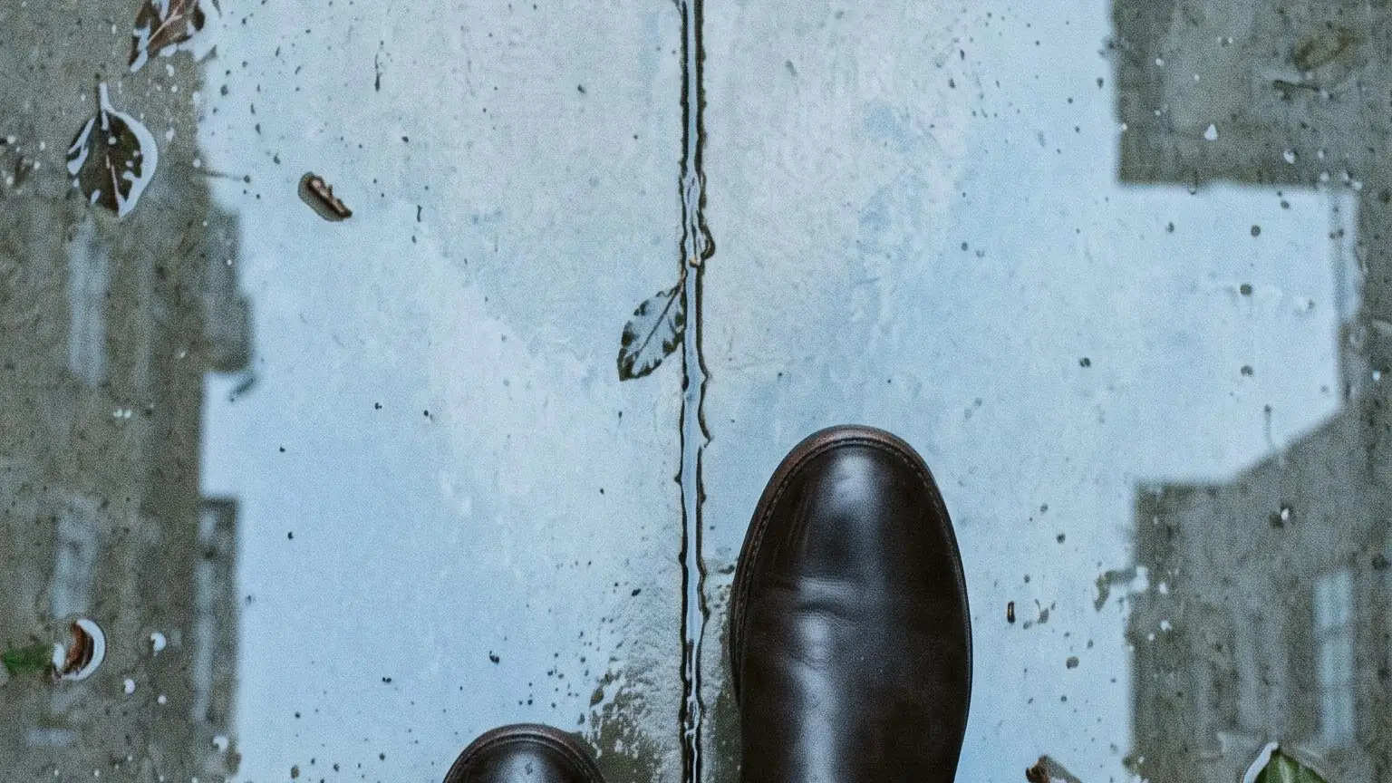 Looking down at a pair of boots mid-stride on a wet pavement