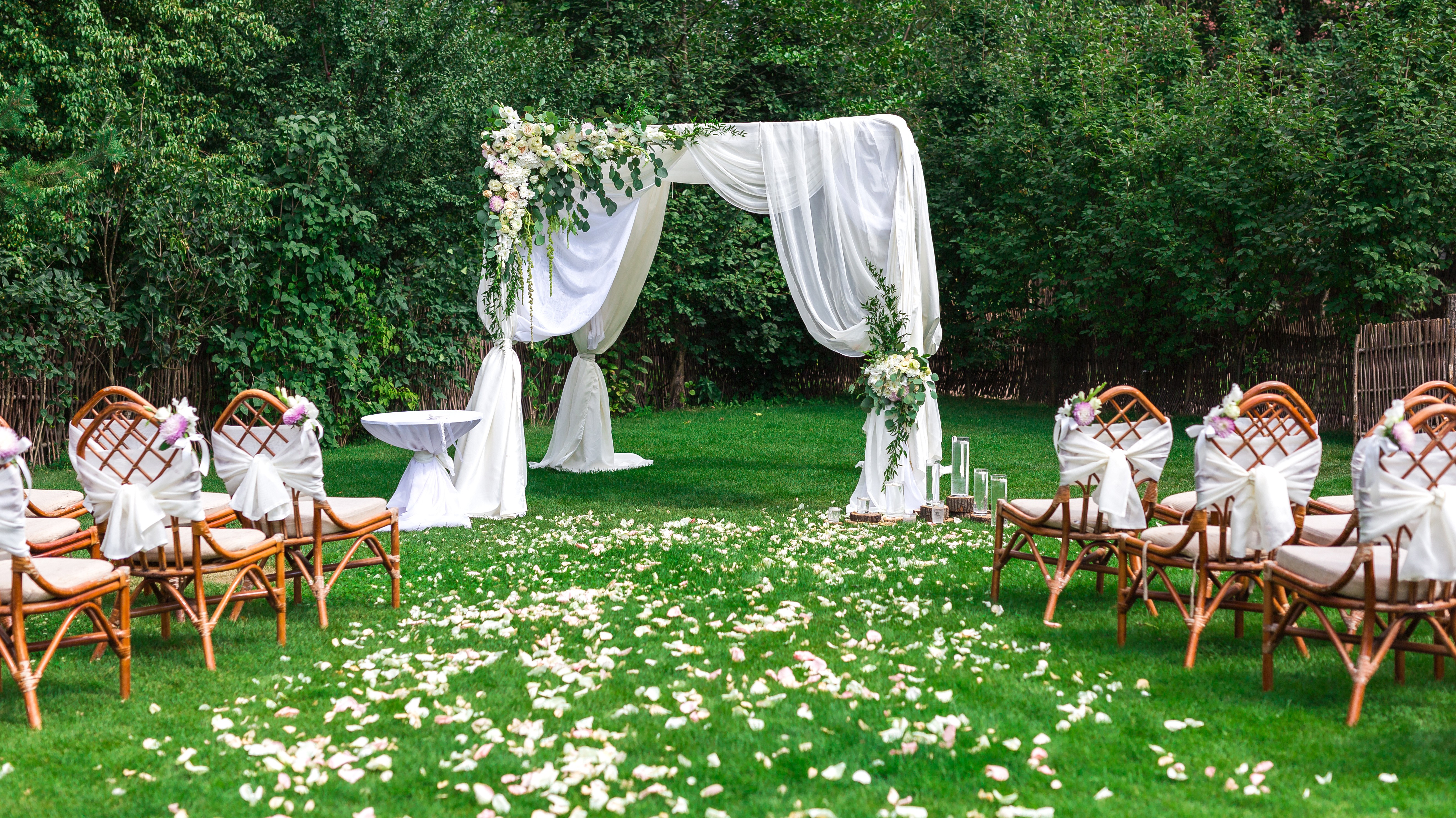A bride and groom hold hands tenderly, the bride's bouquet of dried flowers hanging low. They stand in a softly lit, elegant interior, conveying romance.