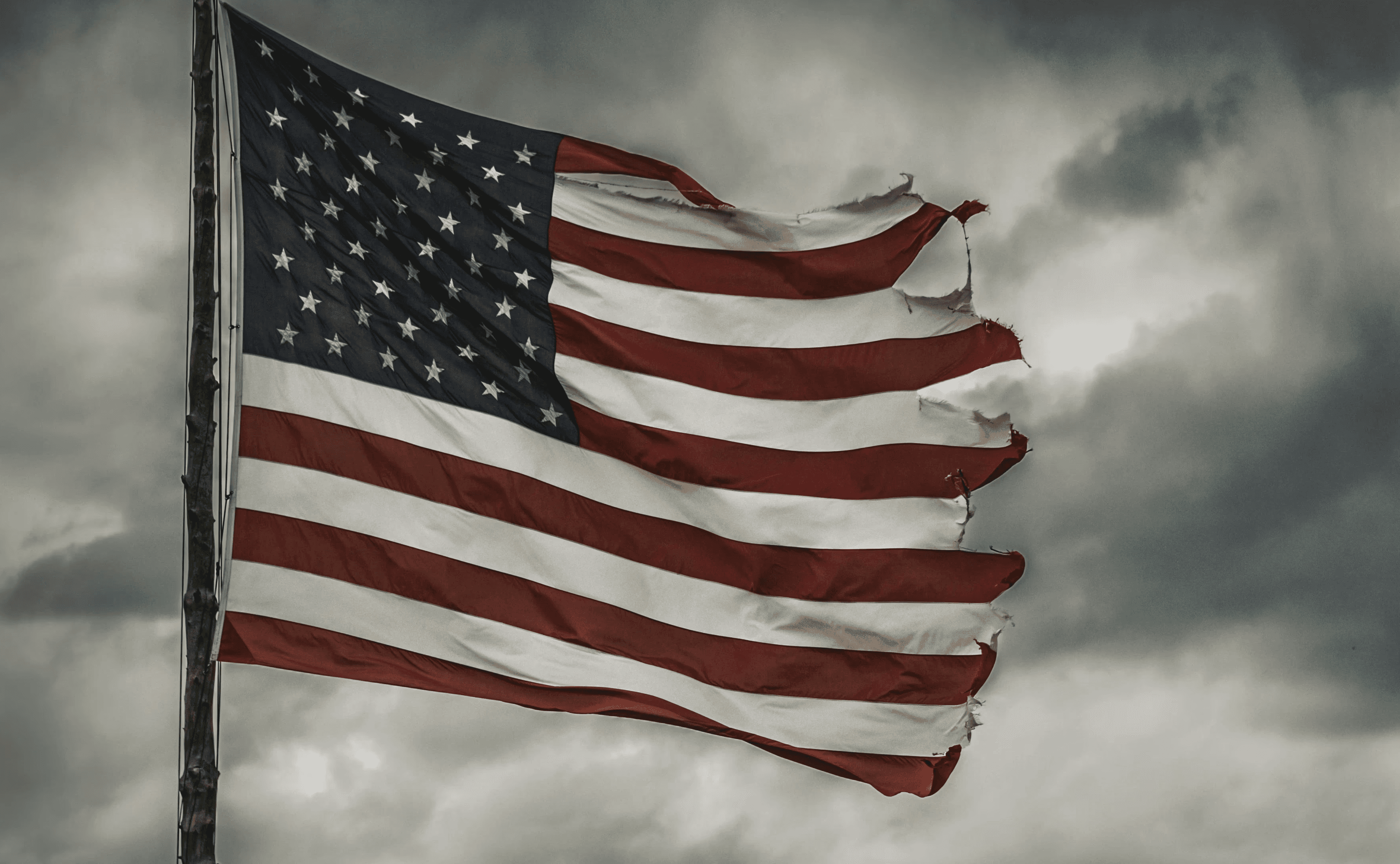 a large american flag flying in a cloudy sky