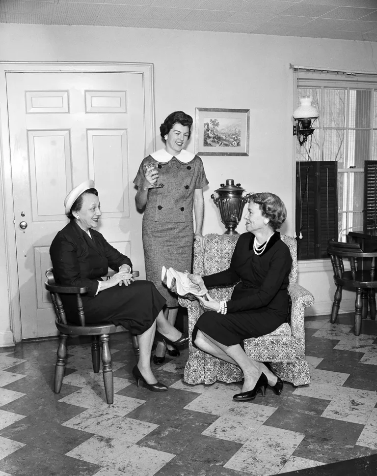 Three women at a 1959 fundraising tea, Mrs Bratten standing at centre