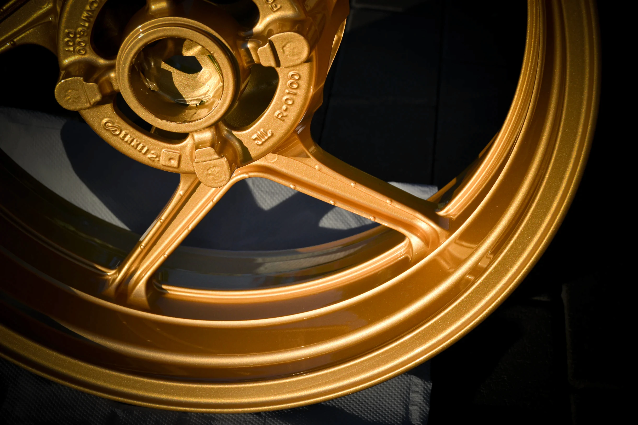 Detail der goldfarbenen Nabenpartie, Speichen und des Felgenrands einer Motorradfelge bei AT Plus.
