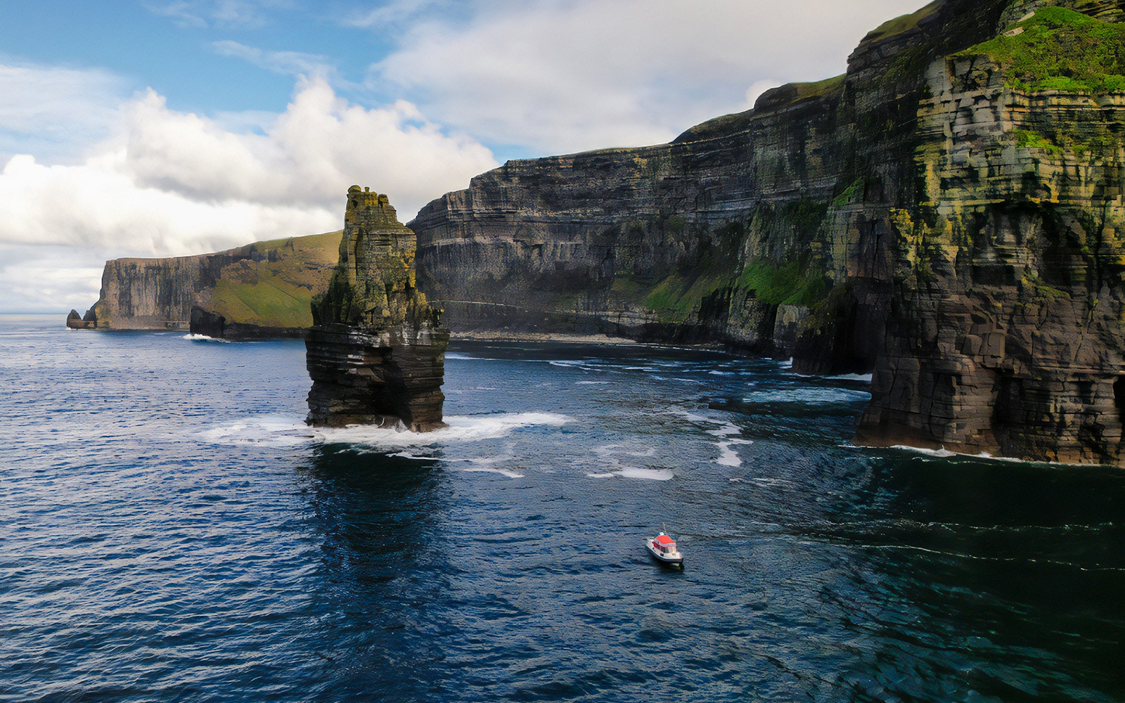 Boat approaching the Cliffs of Moher, Ireland, with sea stack in foreground.