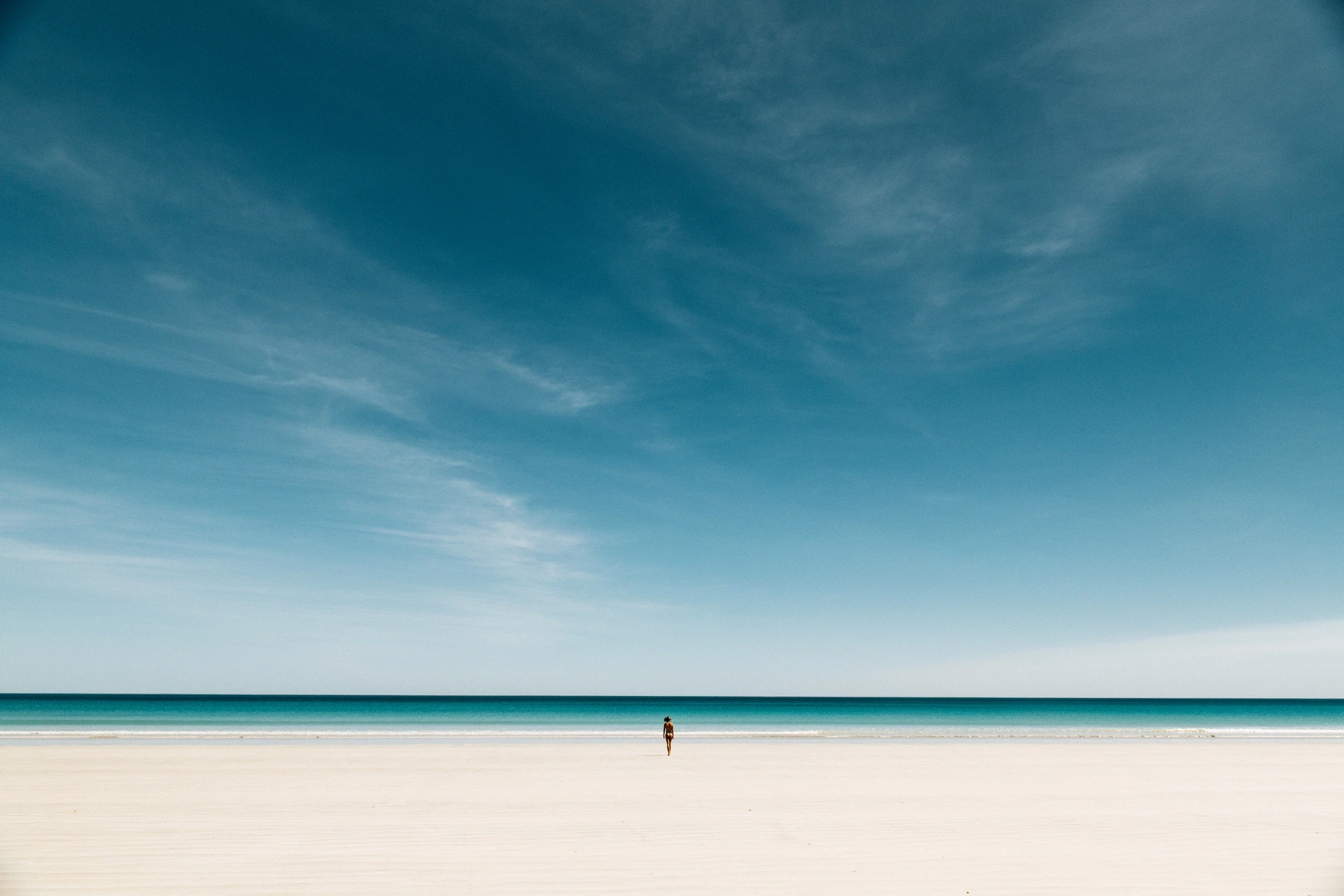 A single figure on a vast pale flat beneath a deep blue sky