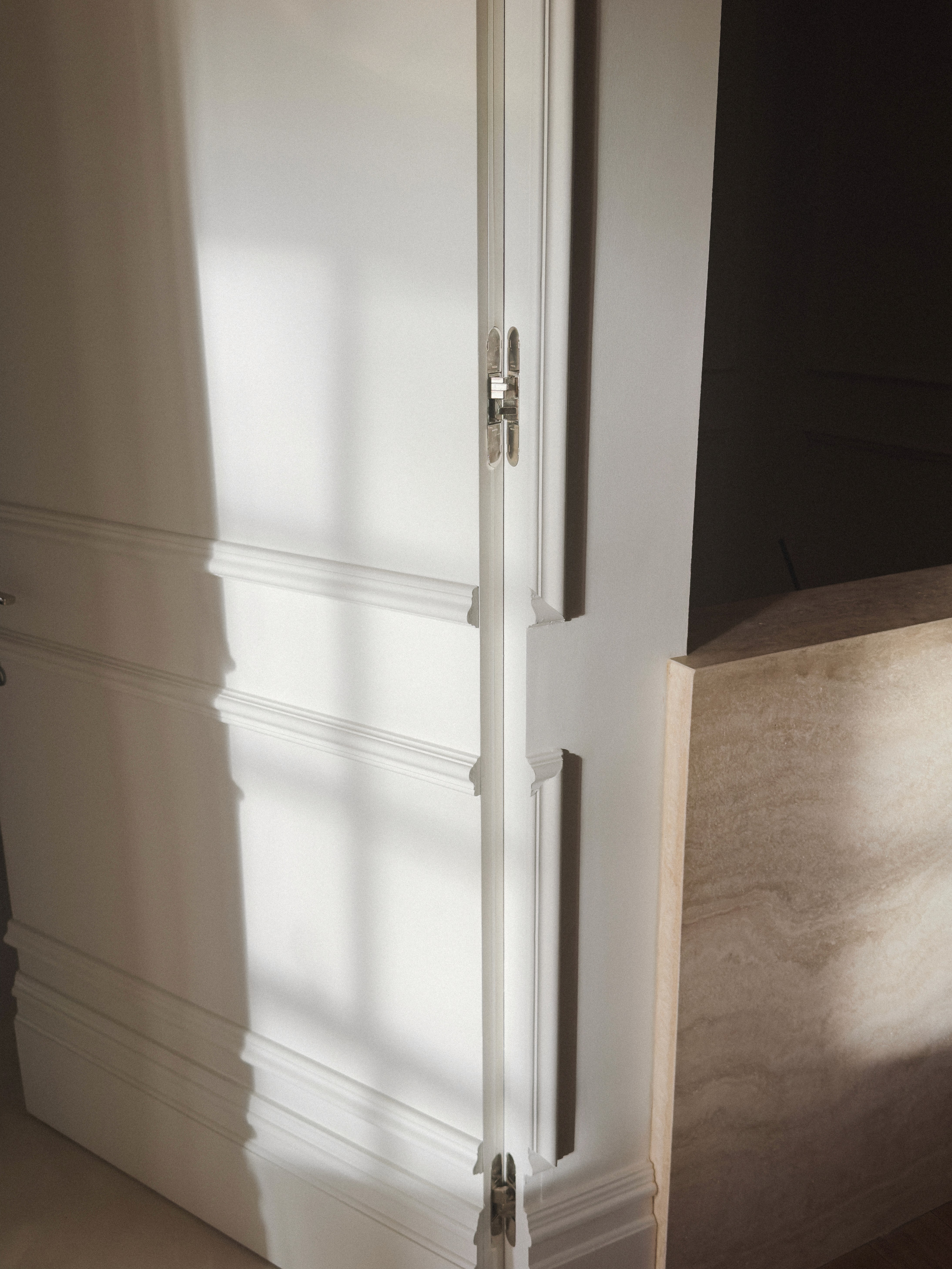 Minimal white wall detail with invisible door with strong sunlight and shadow lines, stone travertin junction